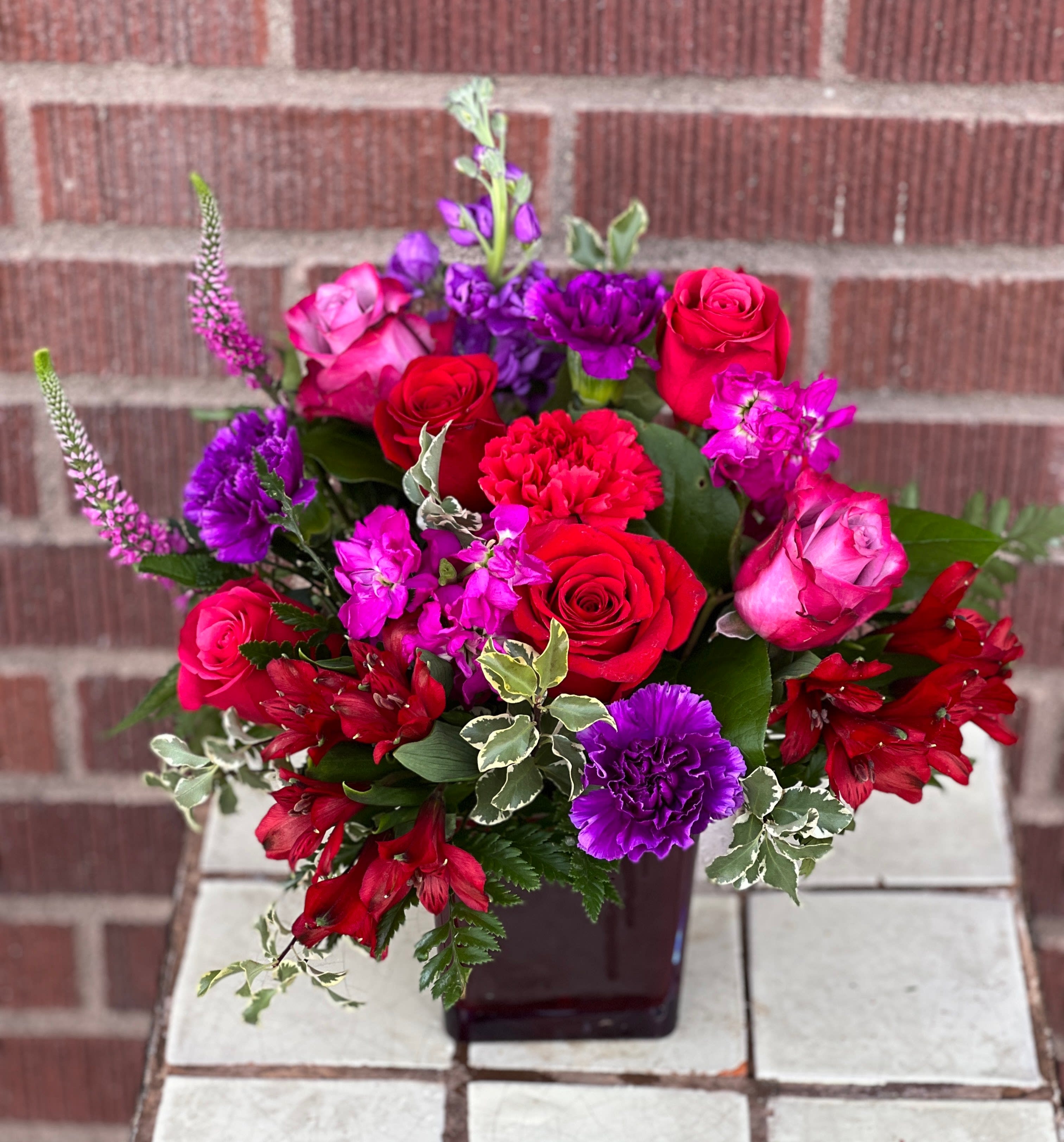 Mixed bouquet of red, pink, and purple flowers in a dark vase