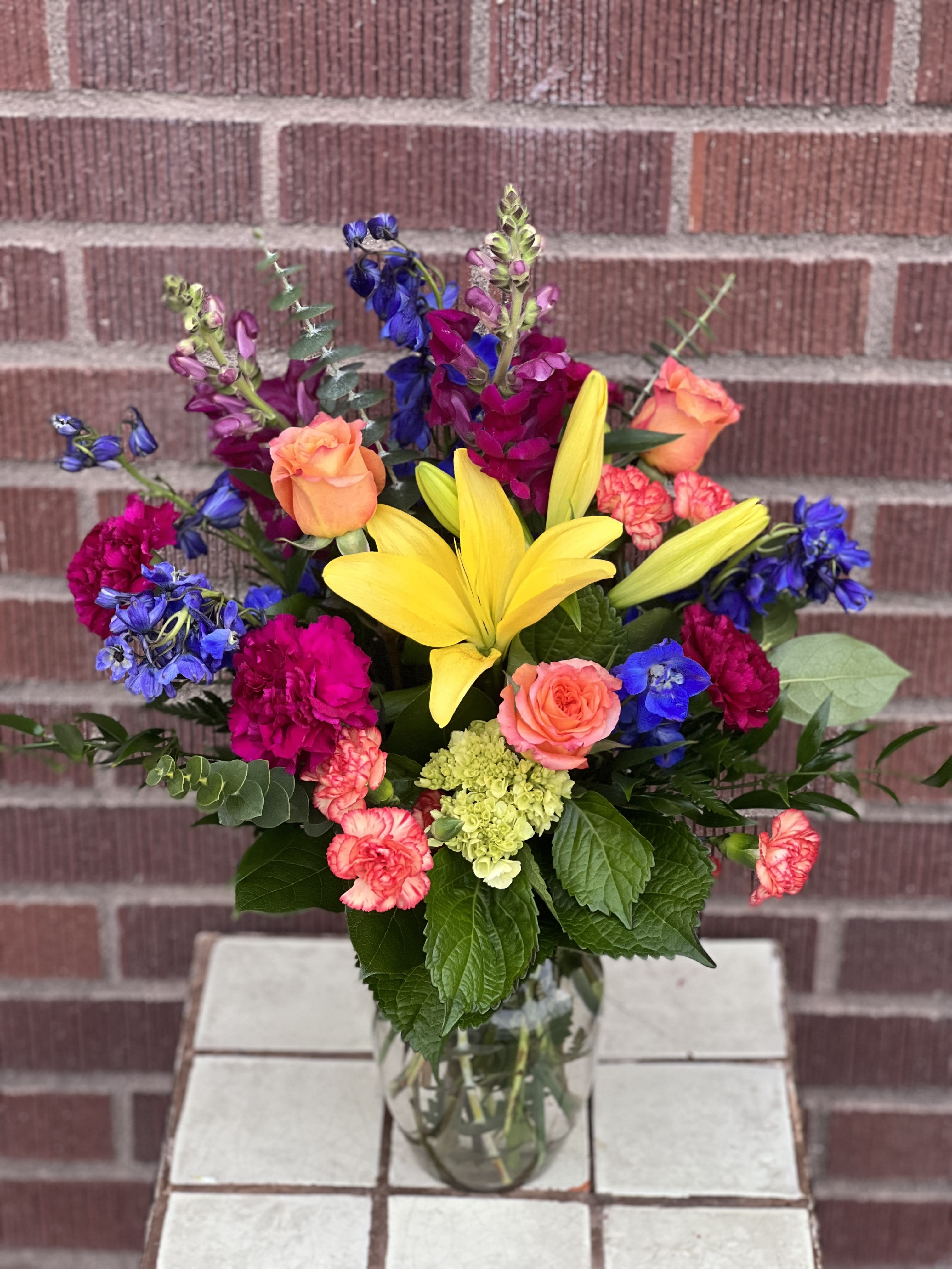 Colorful mixed bouquet with yellow lilies, roses, and carnations in a glass vase