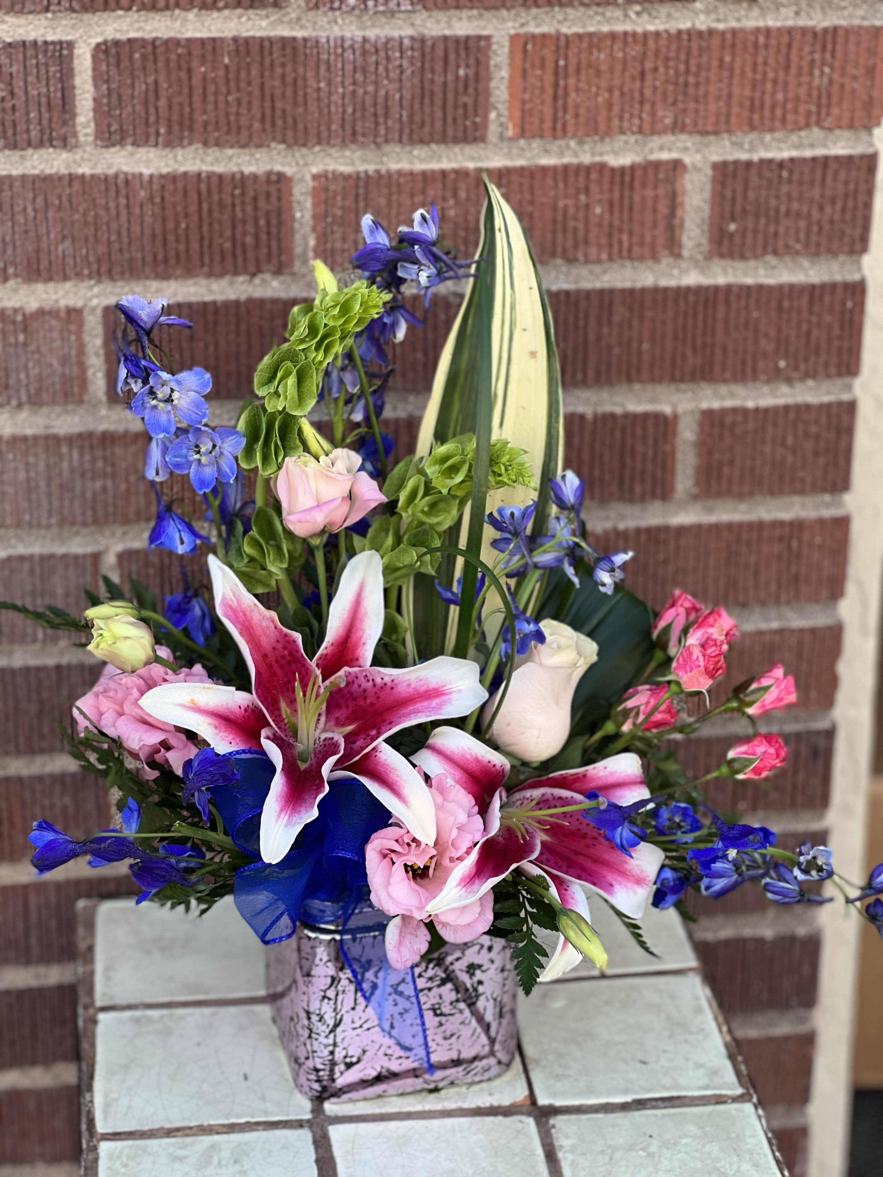 Pink and white lilies with blue flowers in a square vase