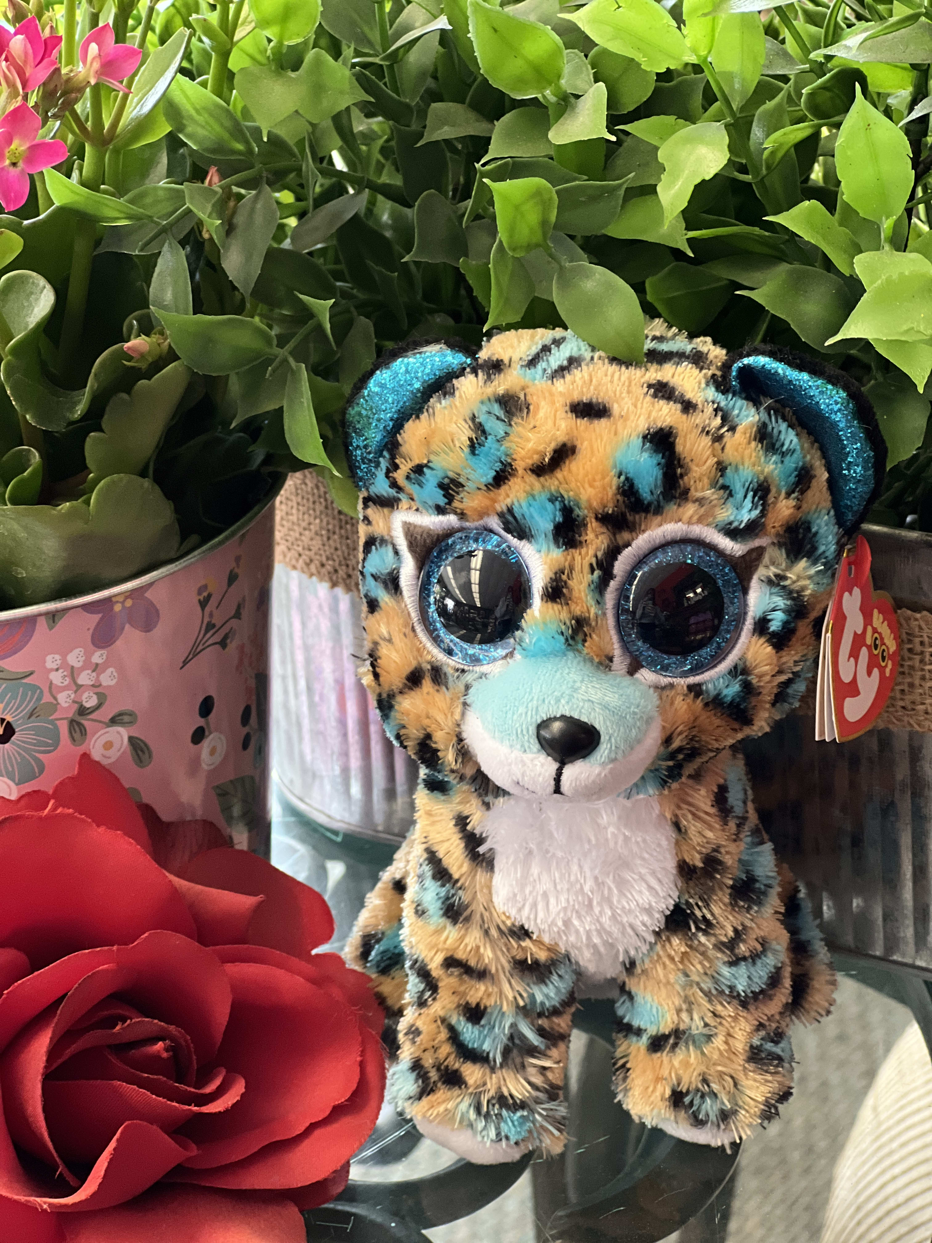 Plush leopard toy beside red roses and a potted plant
