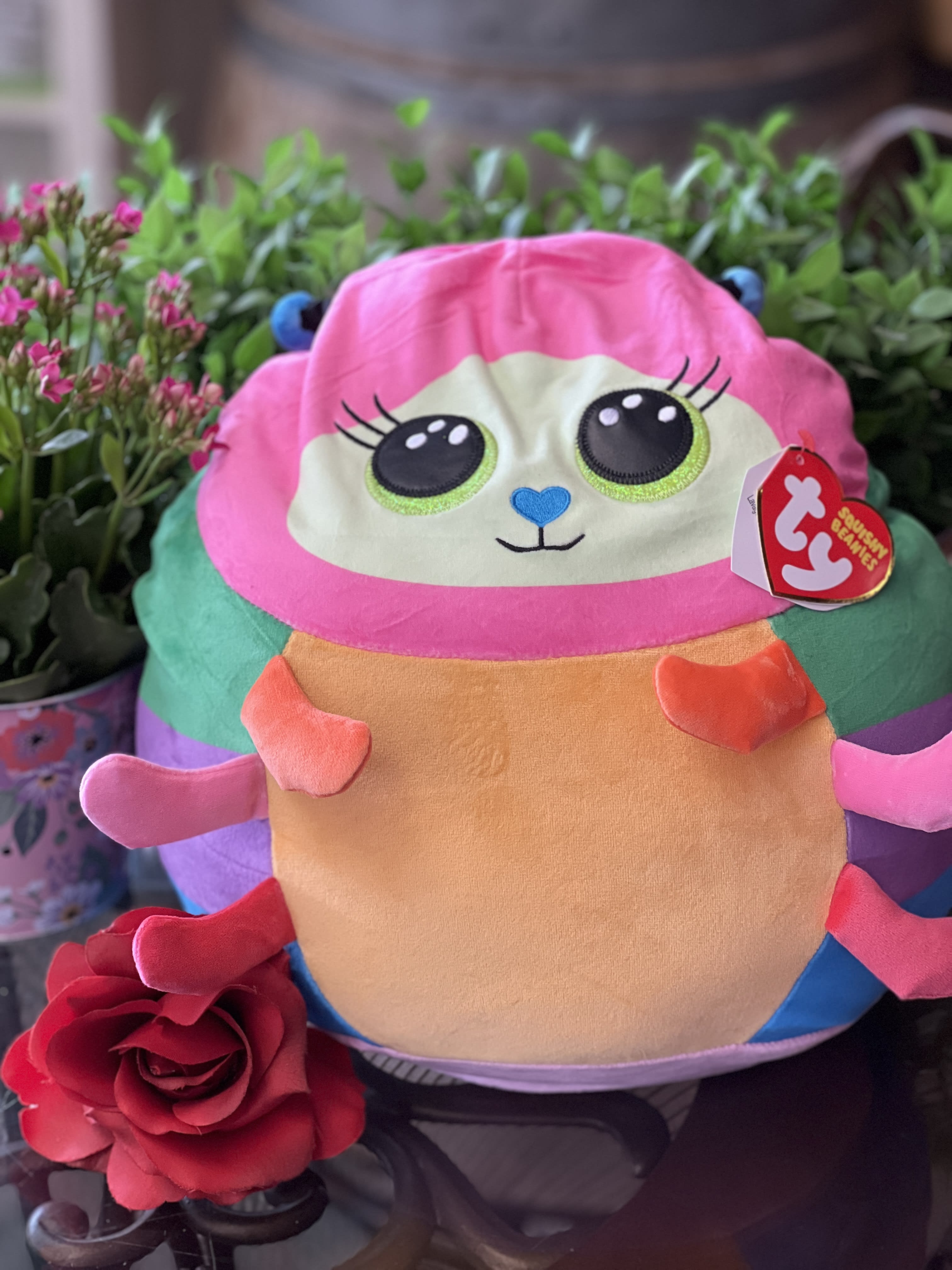 Plush toy with a red rose in front of potted flowers