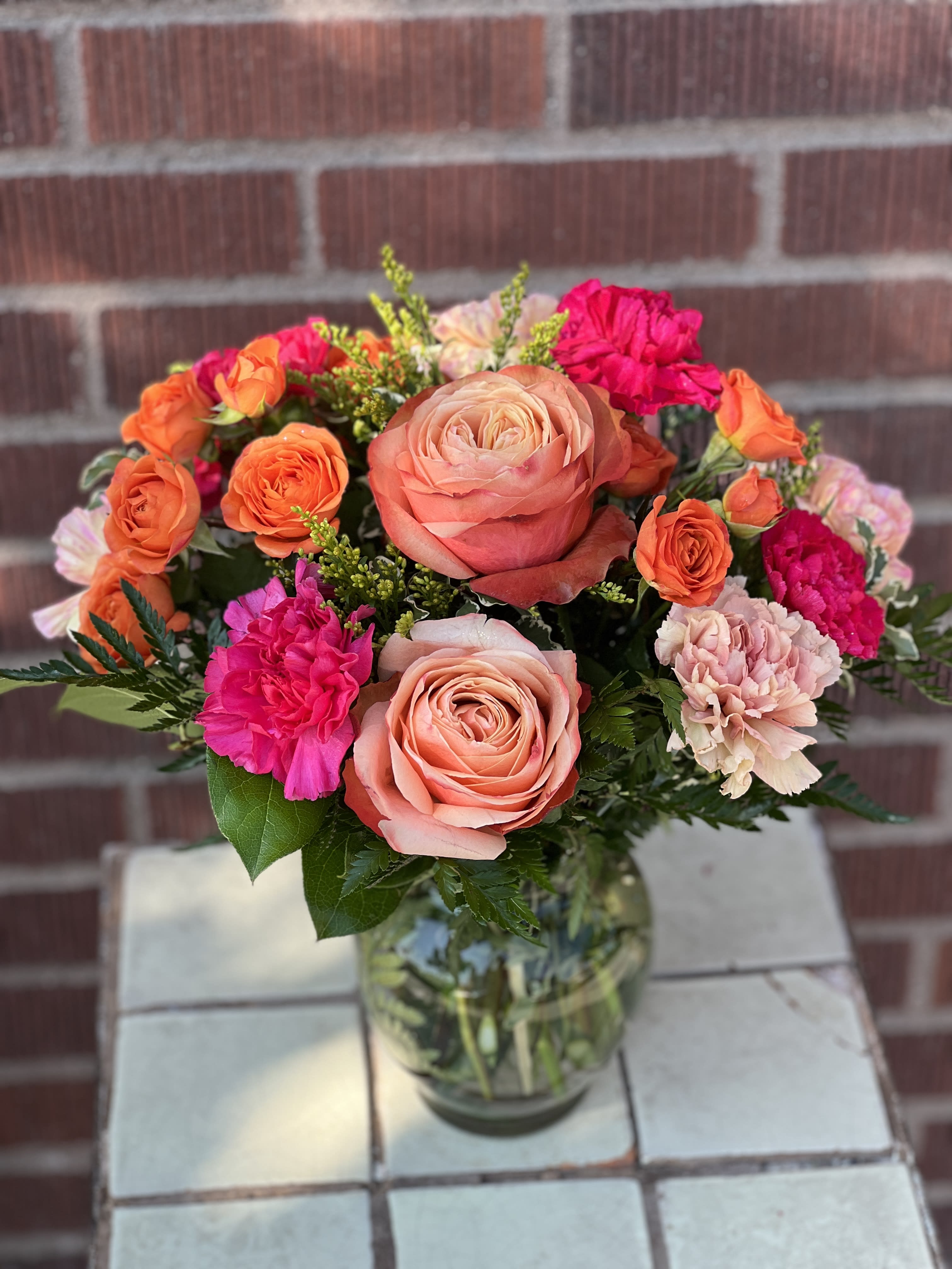 Bouquet of peach and orange roses with pink carnations in a glass vase