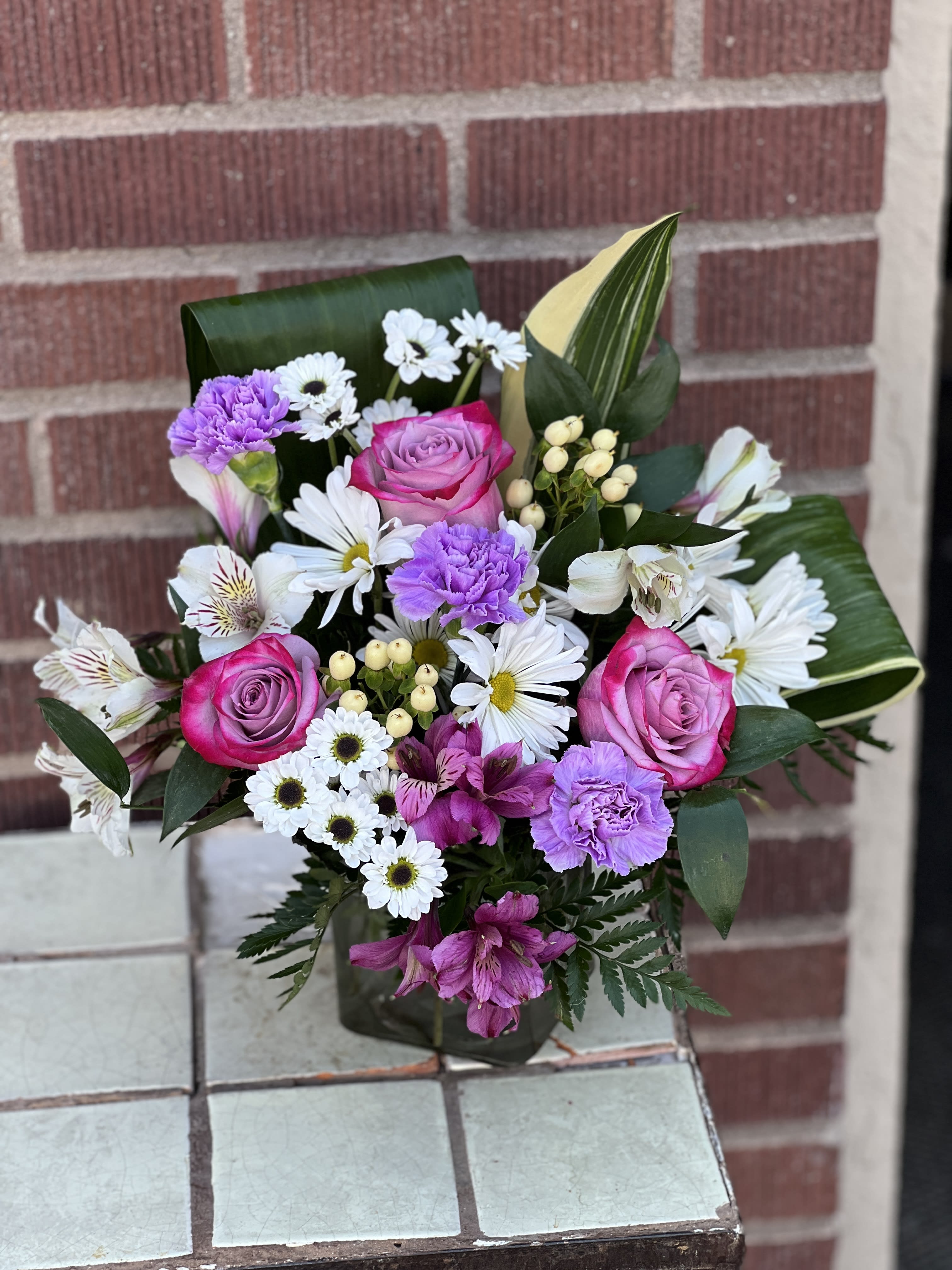 Bouquet of pink roses, white daisies, and purple carnations in a vase