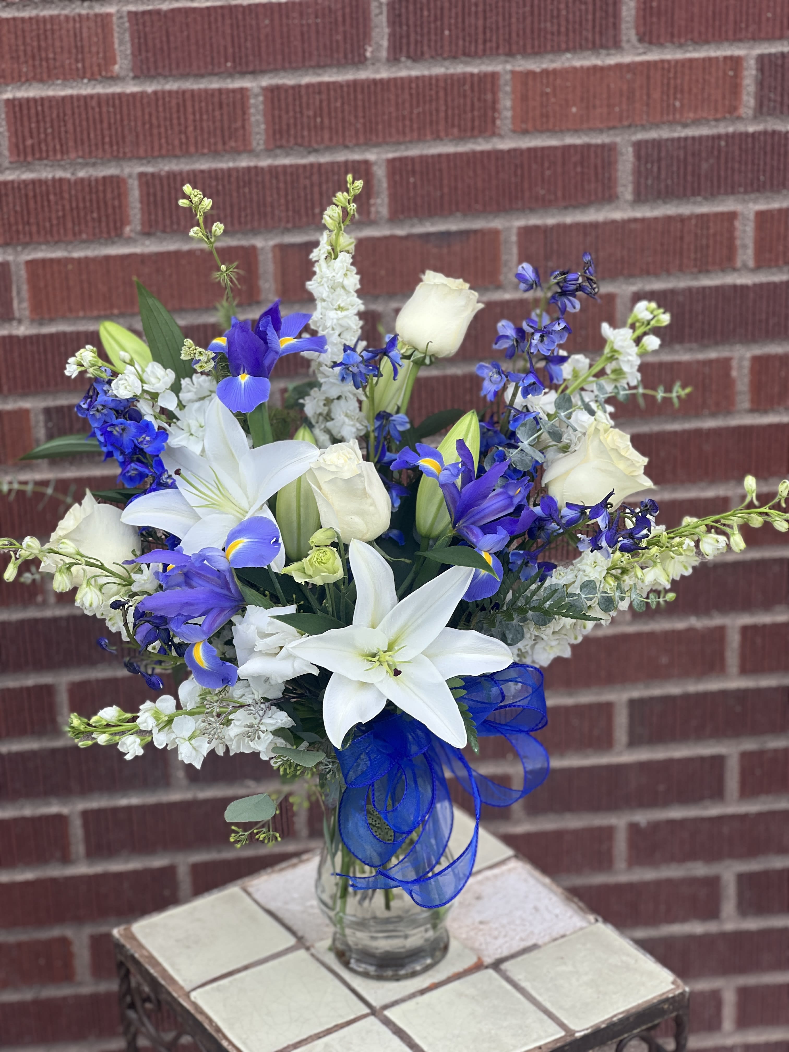 White lilies and blue-purple flowers in a glass vase with a blue ribbon