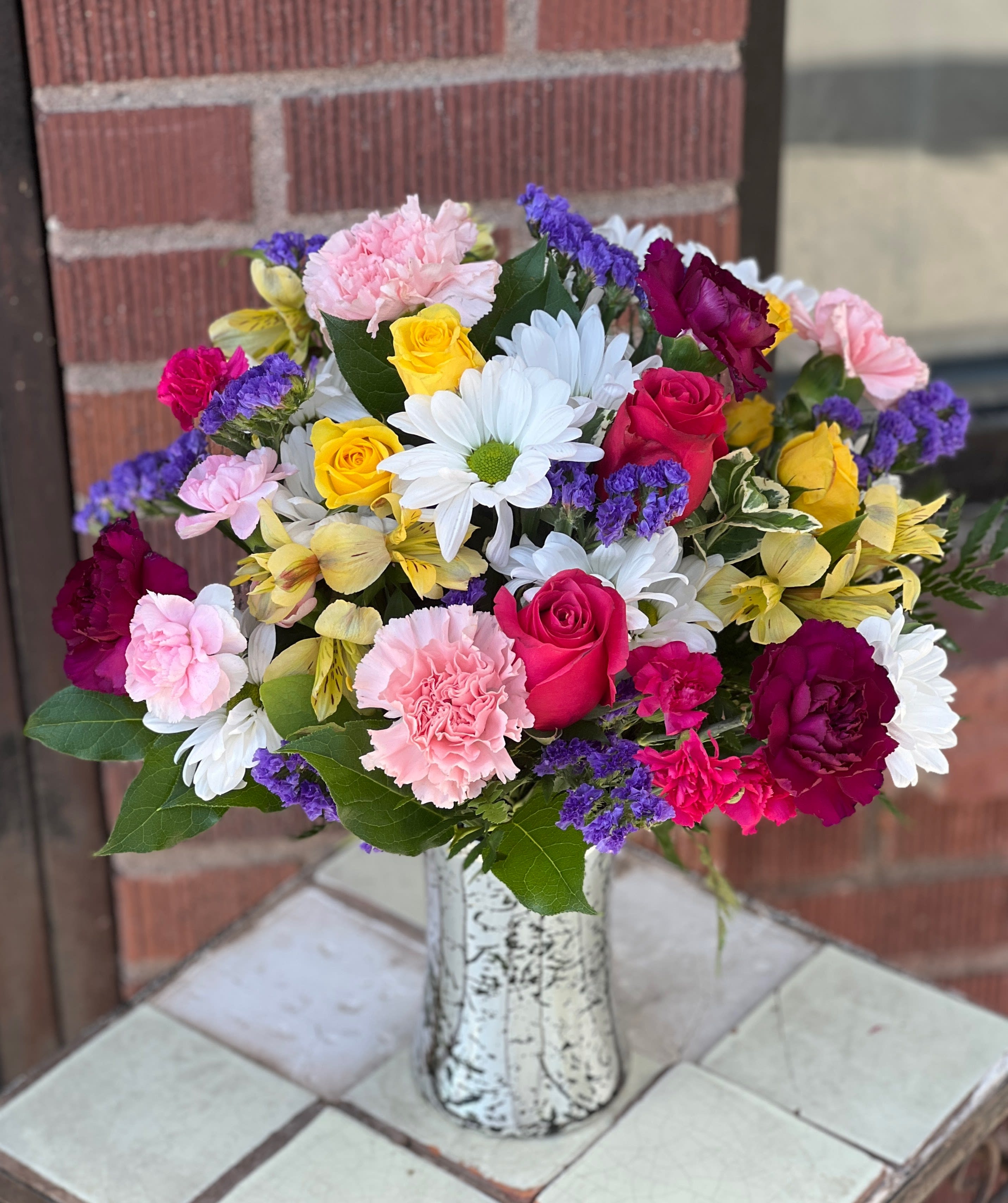 Mixed bouquet of roses, daisies, carnations, and orchids in a white vase