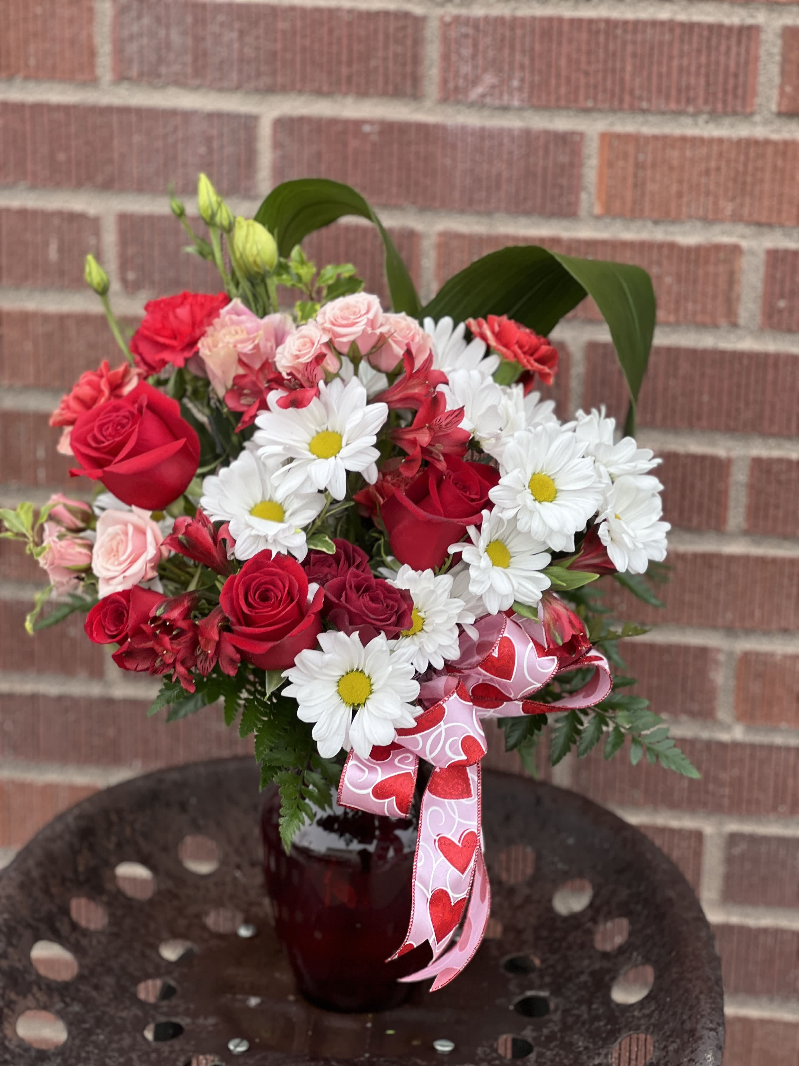 Bouquet of red roses and white daisies in a red vase with a heart ribbon