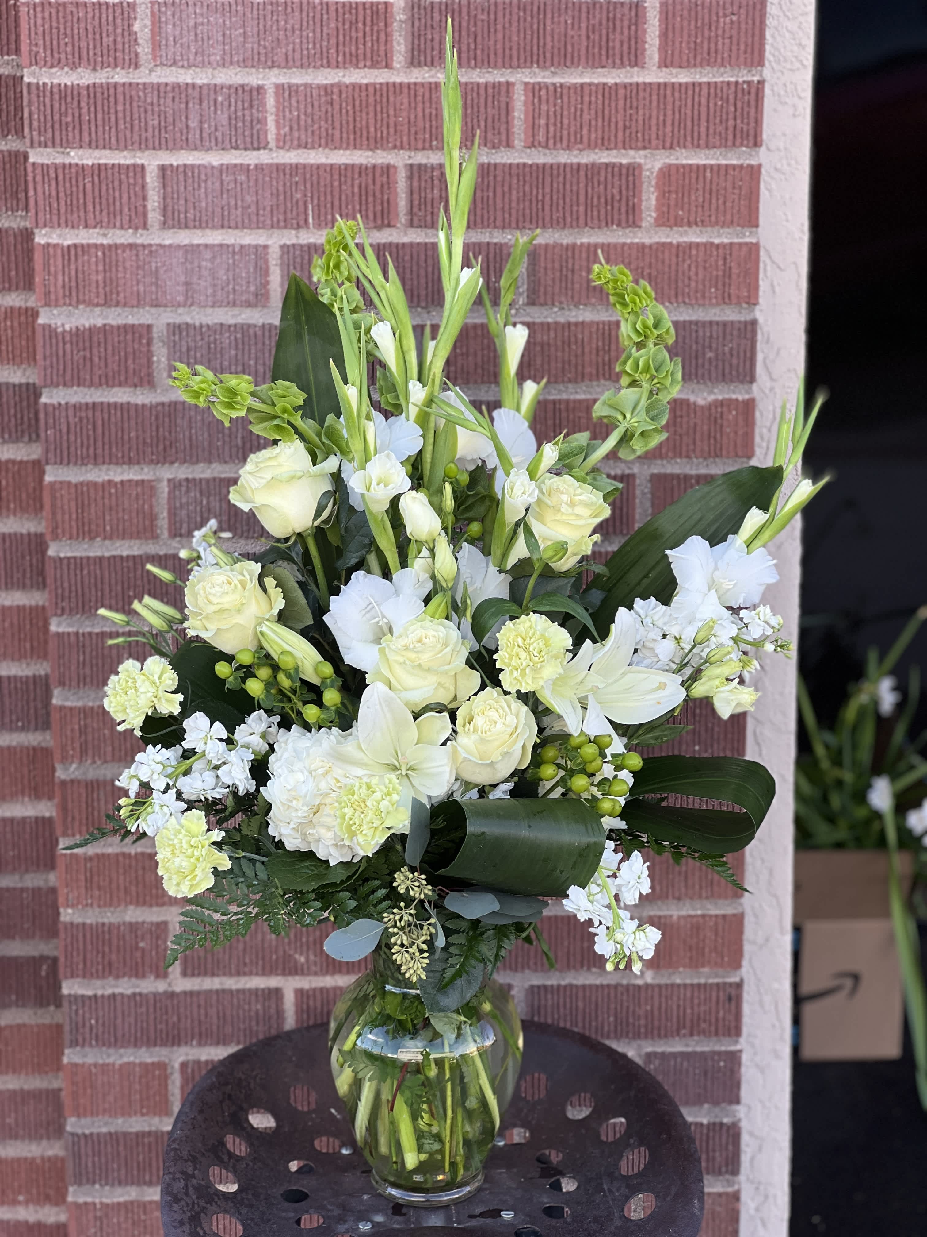 White floral arrangement in a clear glass vase with tall greenery accents