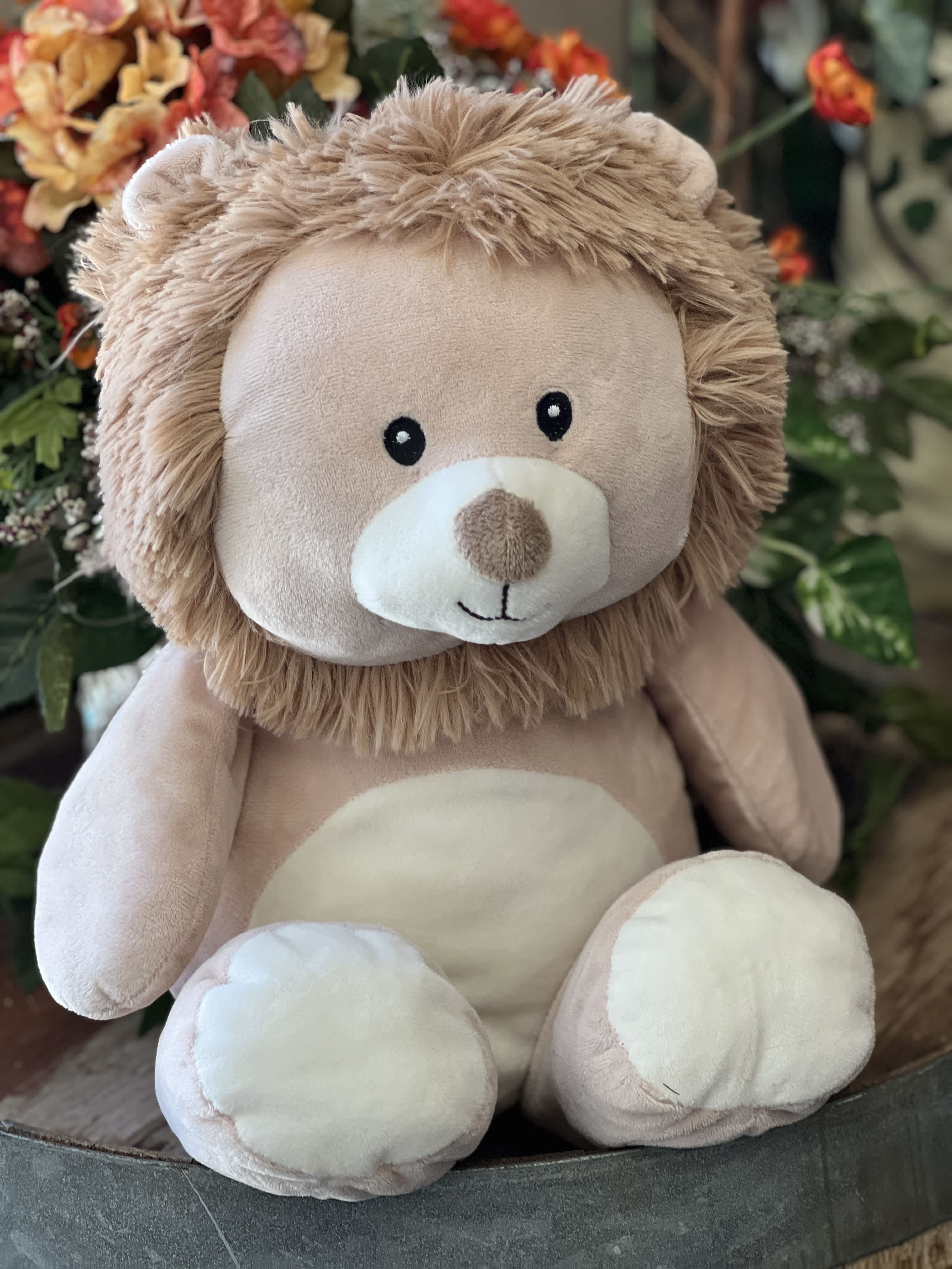 Plush teddy bear with a tan mane sitting in front of flowers