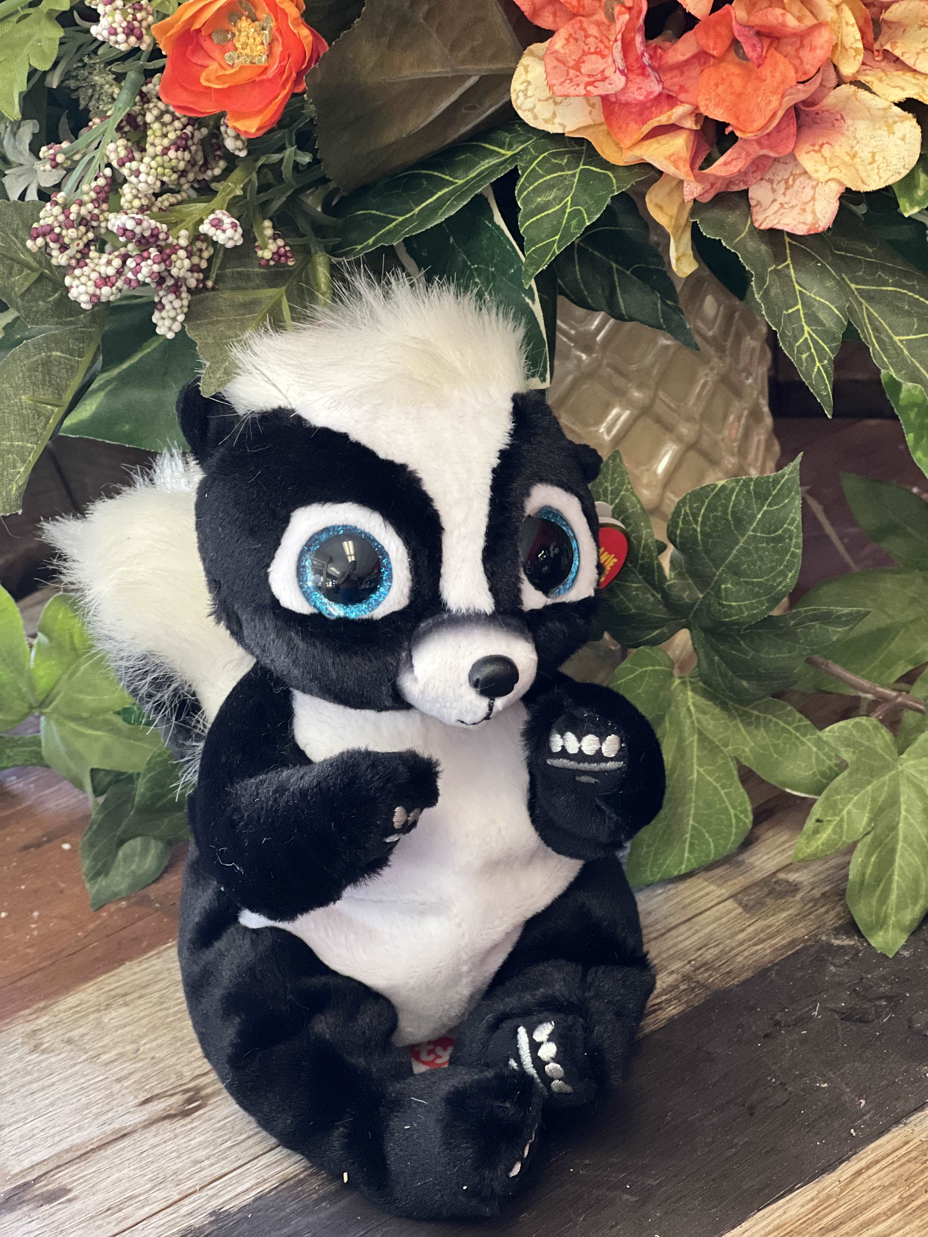Plush skunk toy sitting in front of an artificial floral arrangement