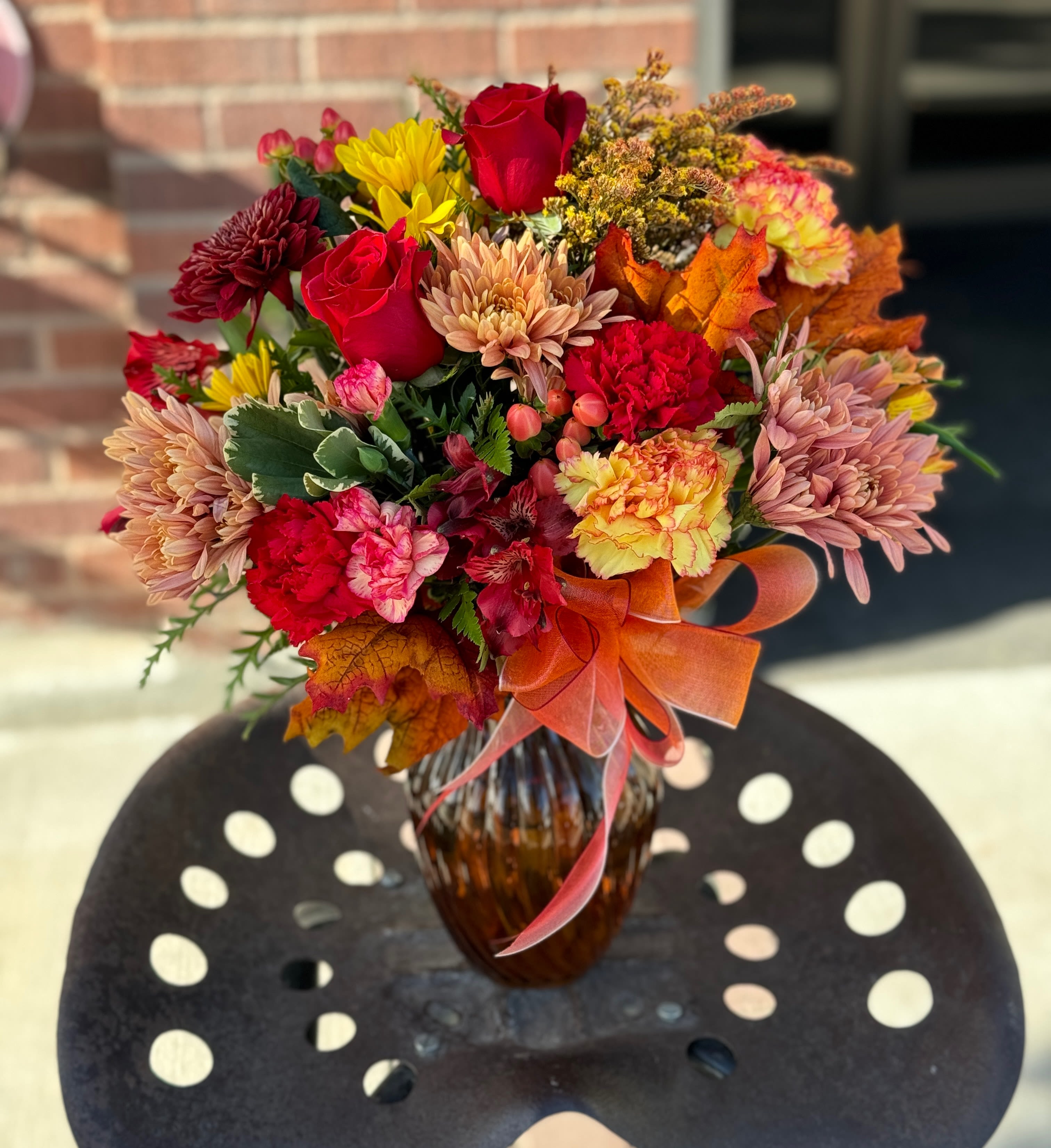 Autumn bouquet of red roses, chrysanthemums, and carnations in a glass vase