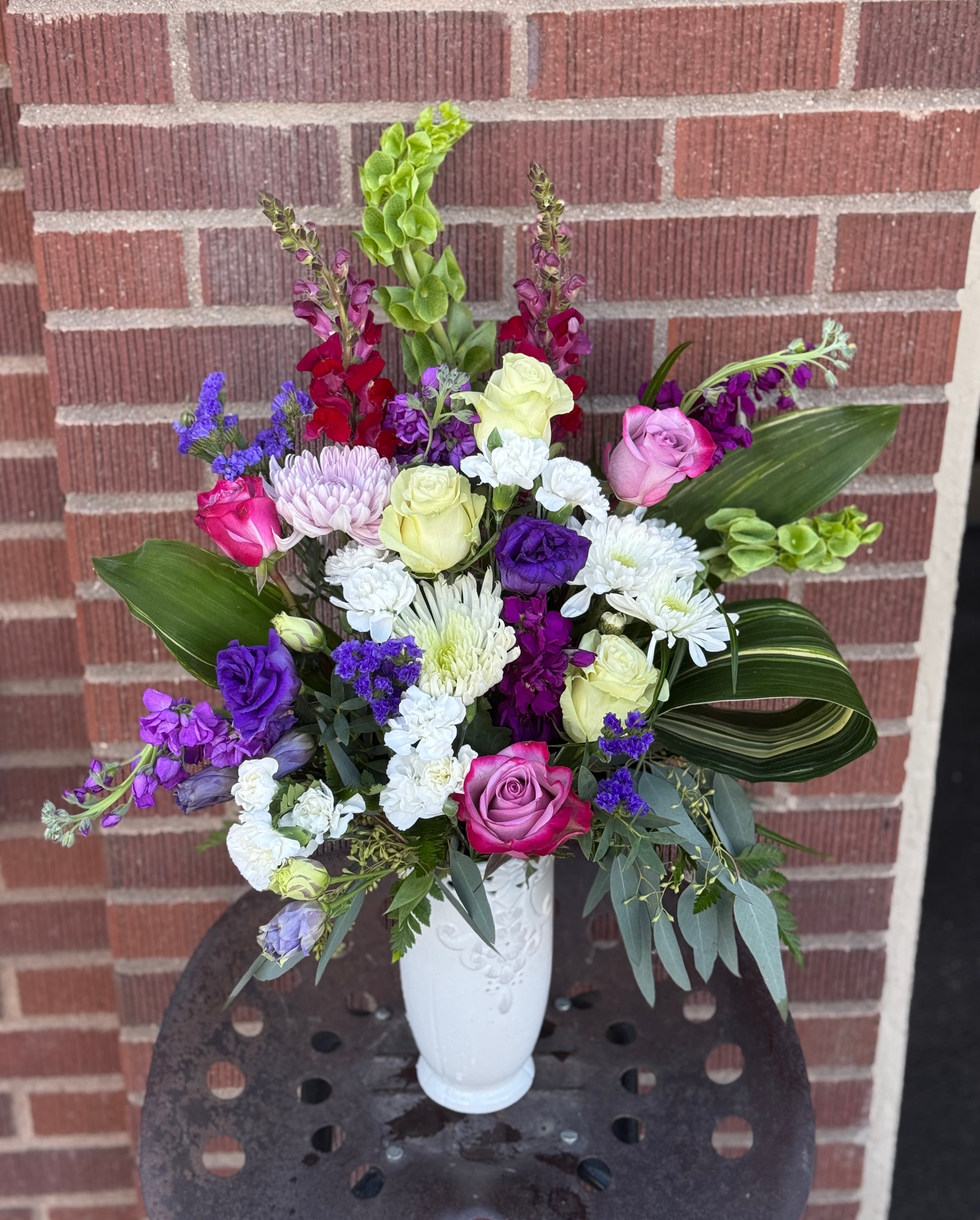 Mixed bouquet of roses, chrysanthemums, and purple flowers in a white vase