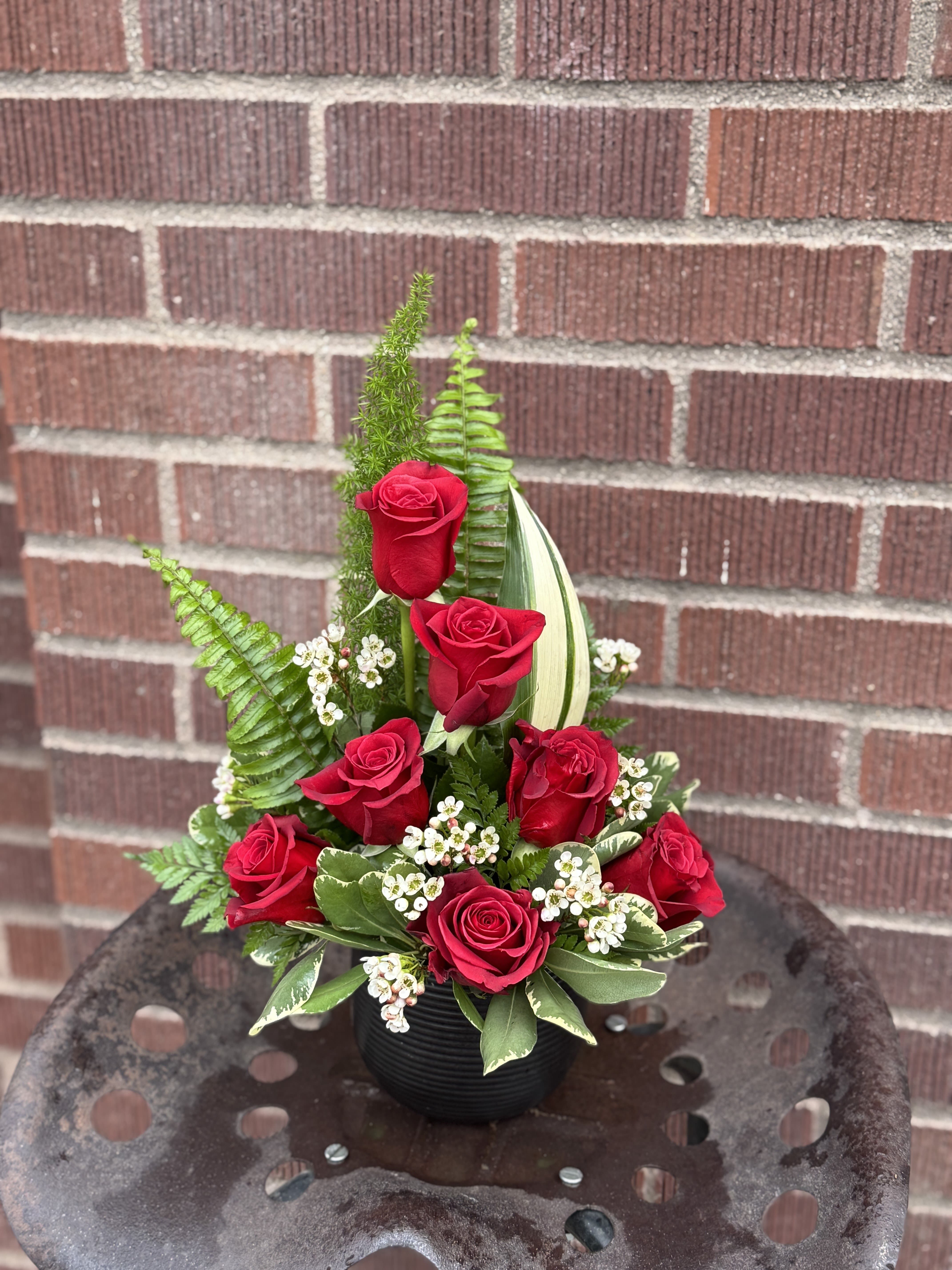 Red roses arranged in a black vase with greenery and white filler flowers