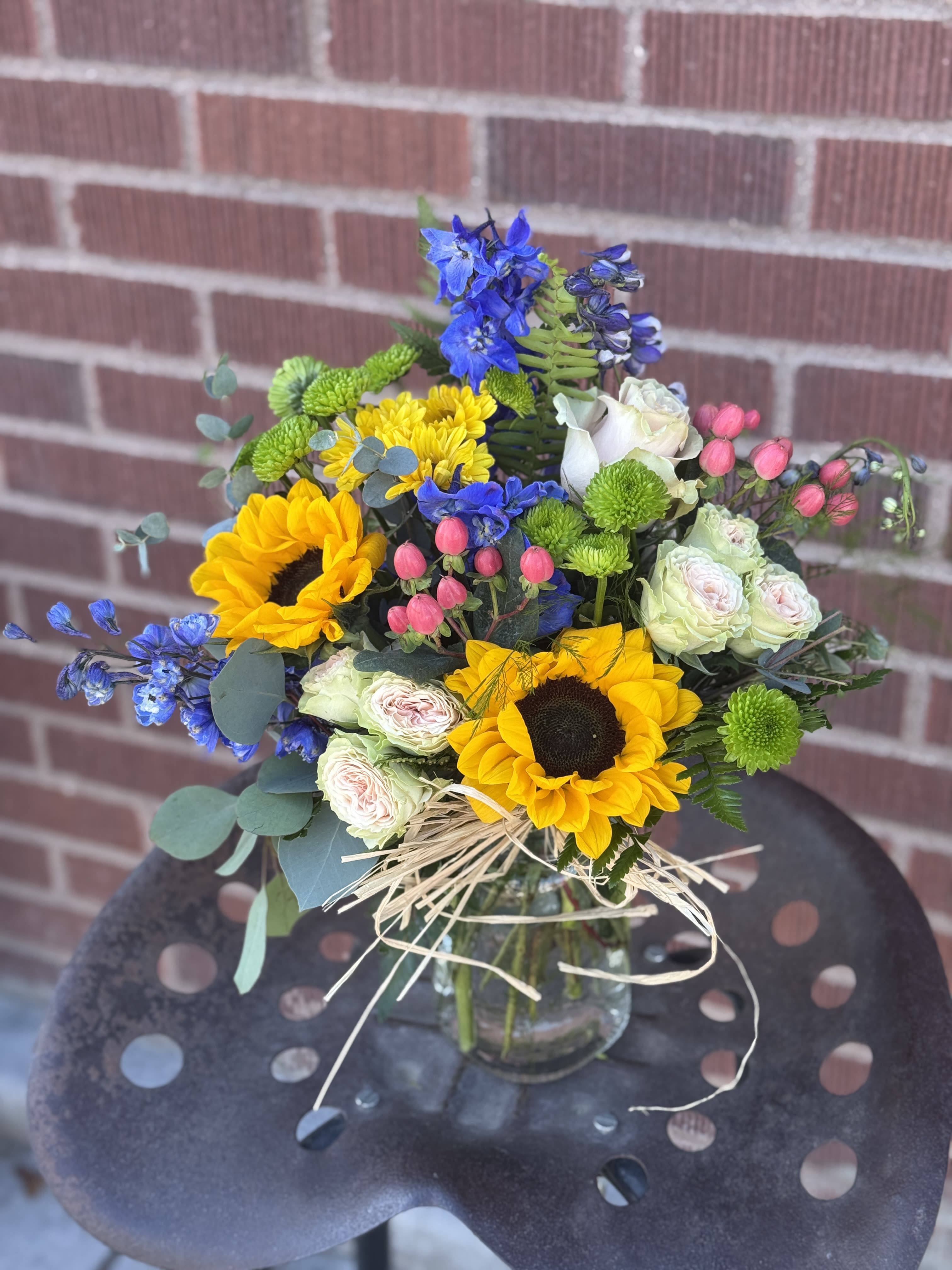 Mixed bouquet with sunflowers, blue flowers, and pale roses in a glass vase