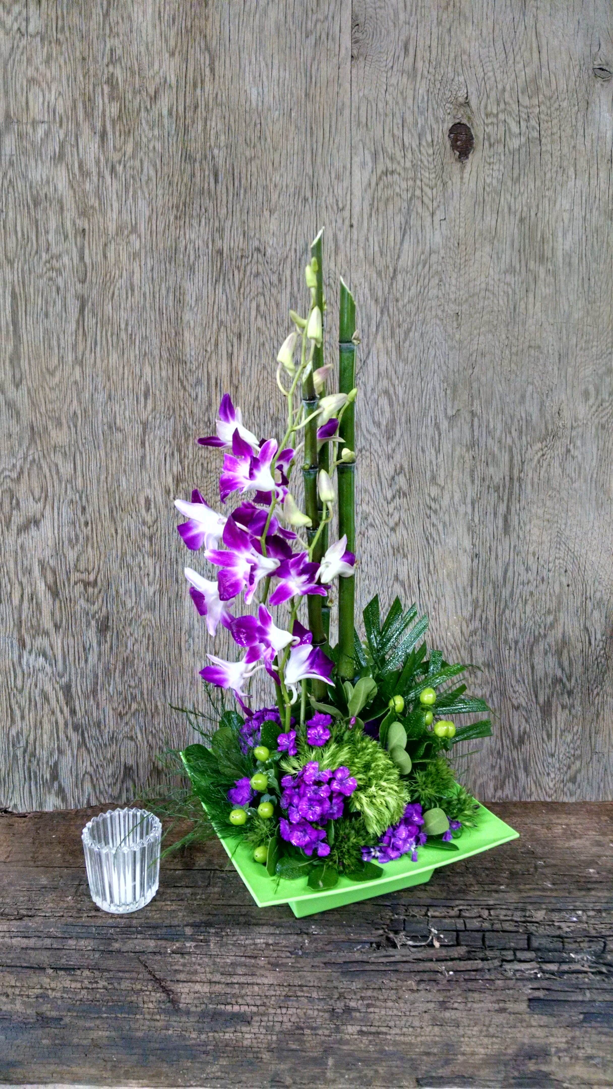 Purple orchids in a green square vase with a small glass candle holder