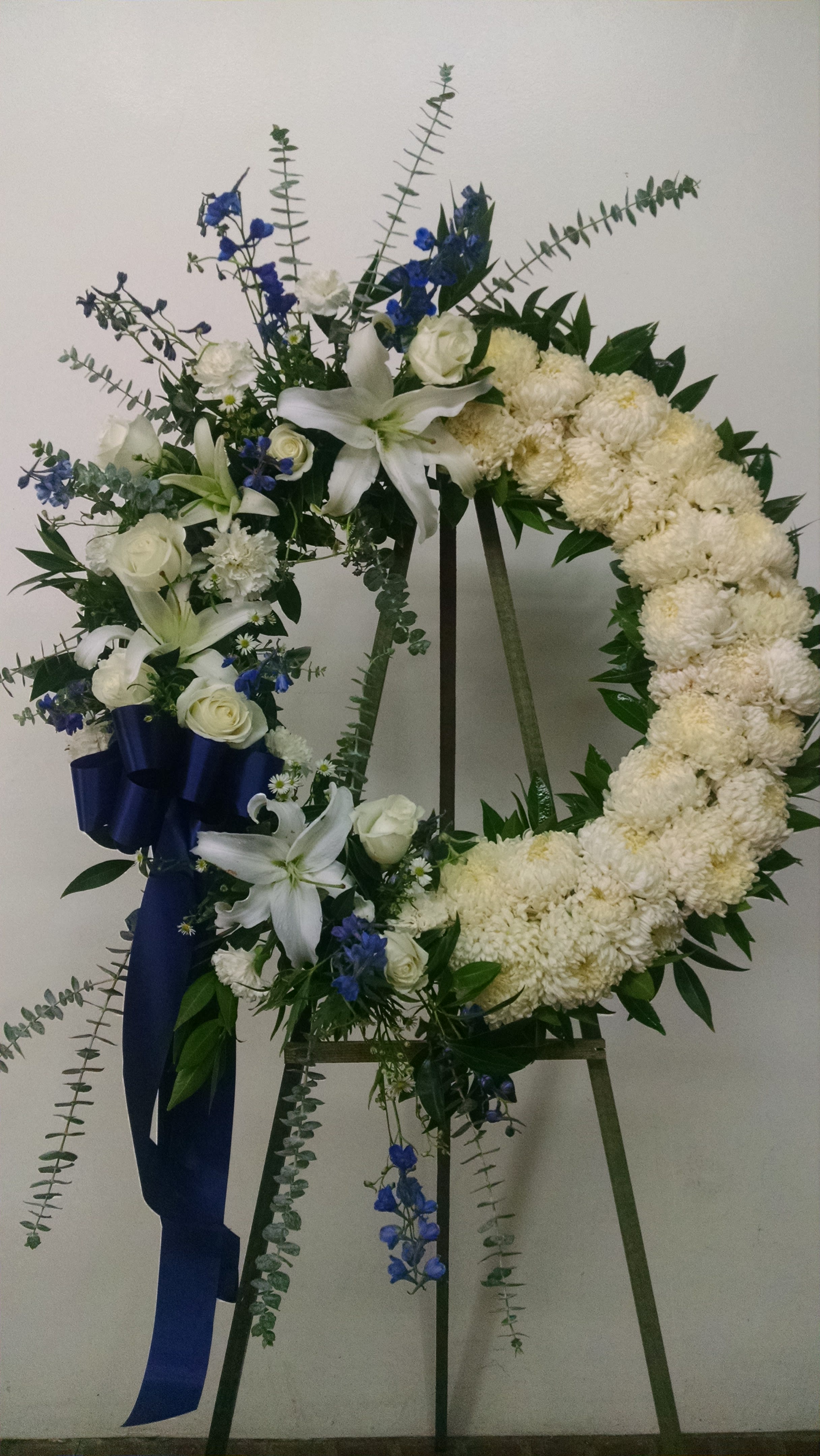 White floral wreath on an easel with blue ribbon accents