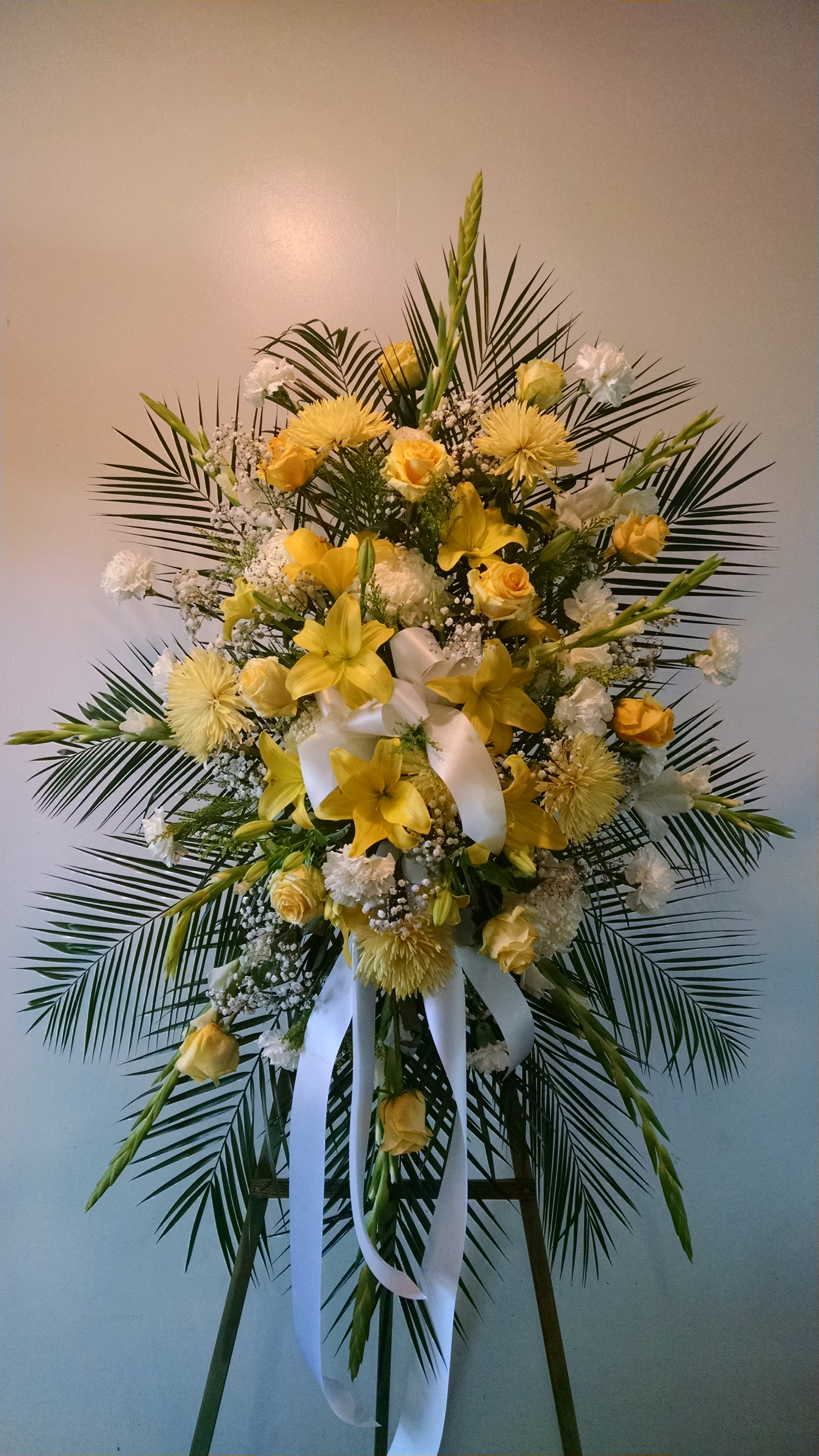 Standing floral spray with yellow lilies and roses on a white ribboned easel