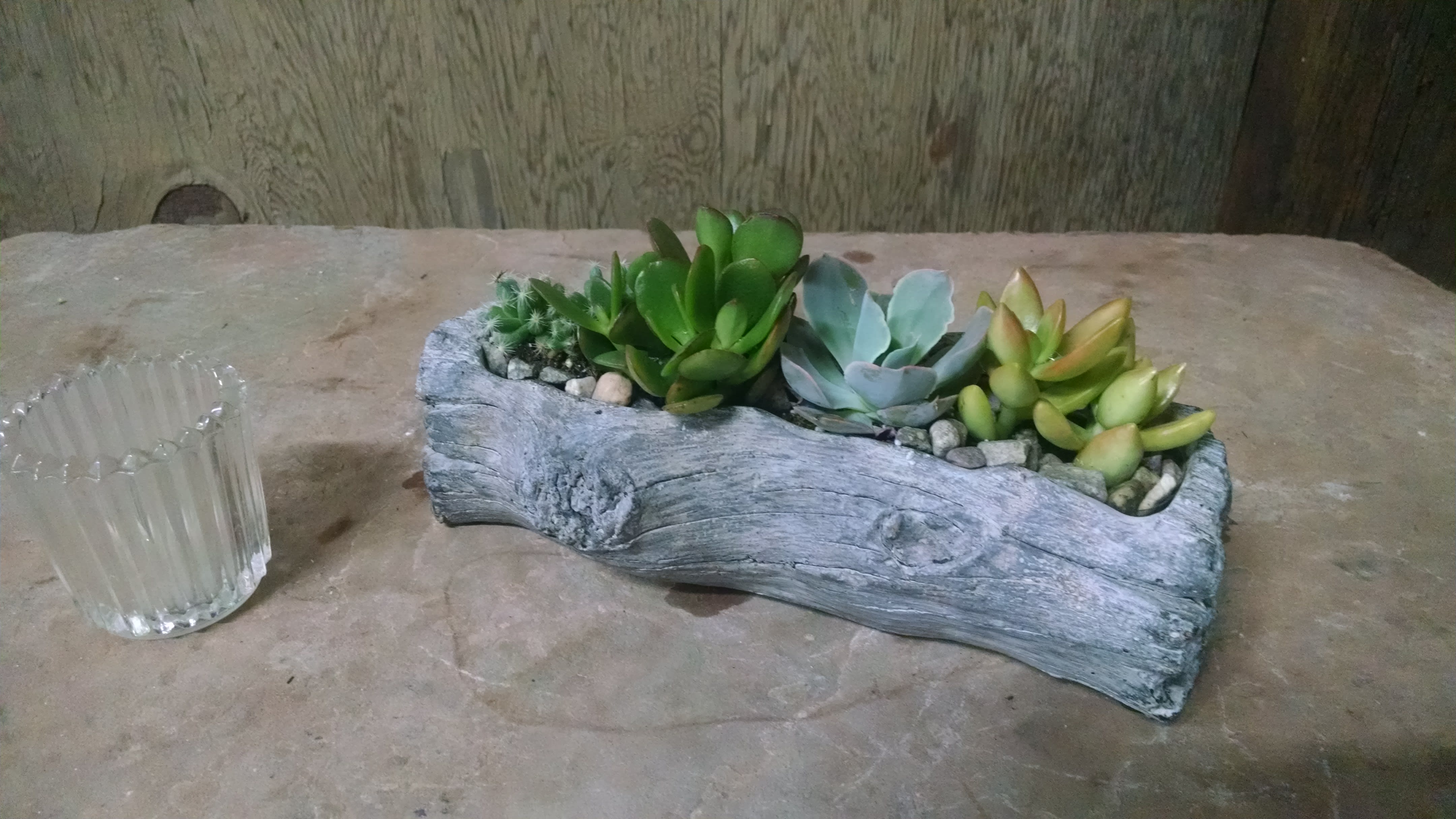 Succulent arrangement in a faux wood planter beside a clear glass votive holder