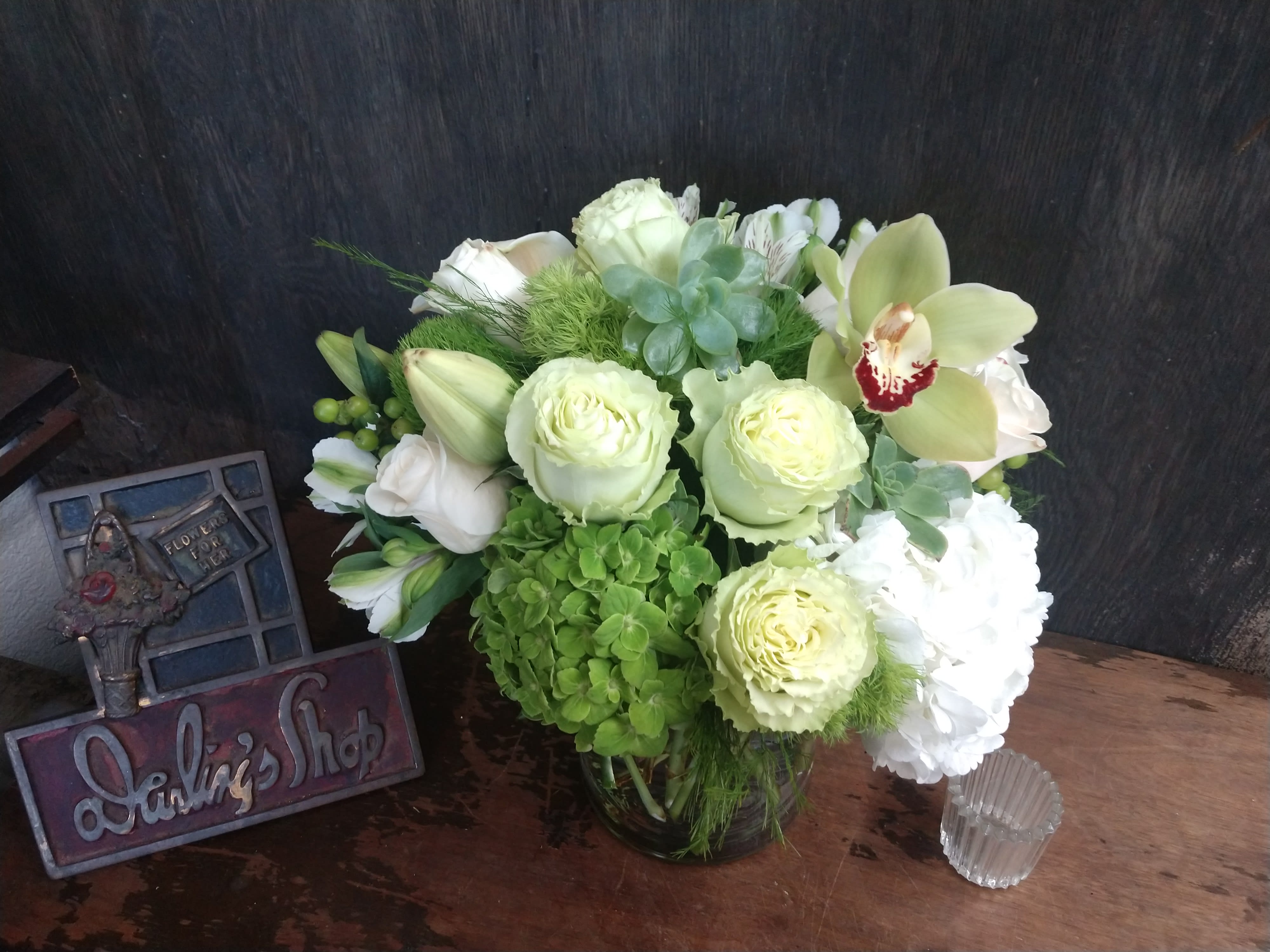 Green and white floral arrangement in a glass vase with orchids and roses