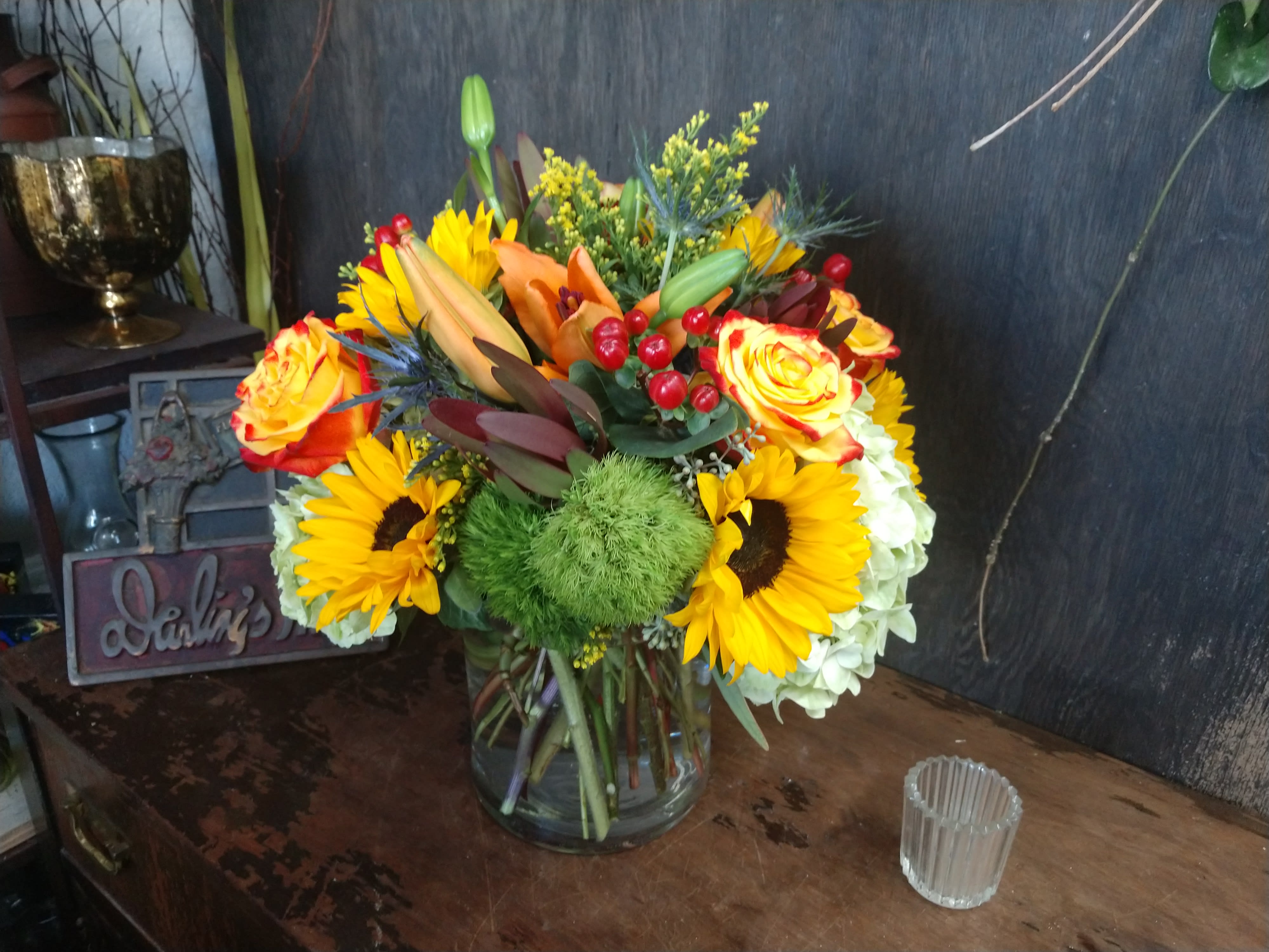 Mixed bouquet in a clear glass vase with sunflowers, roses, and lilies