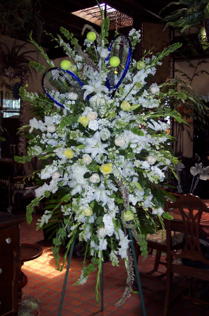 Large white floral standing arrangement with blue tennis rackets and tennis balls