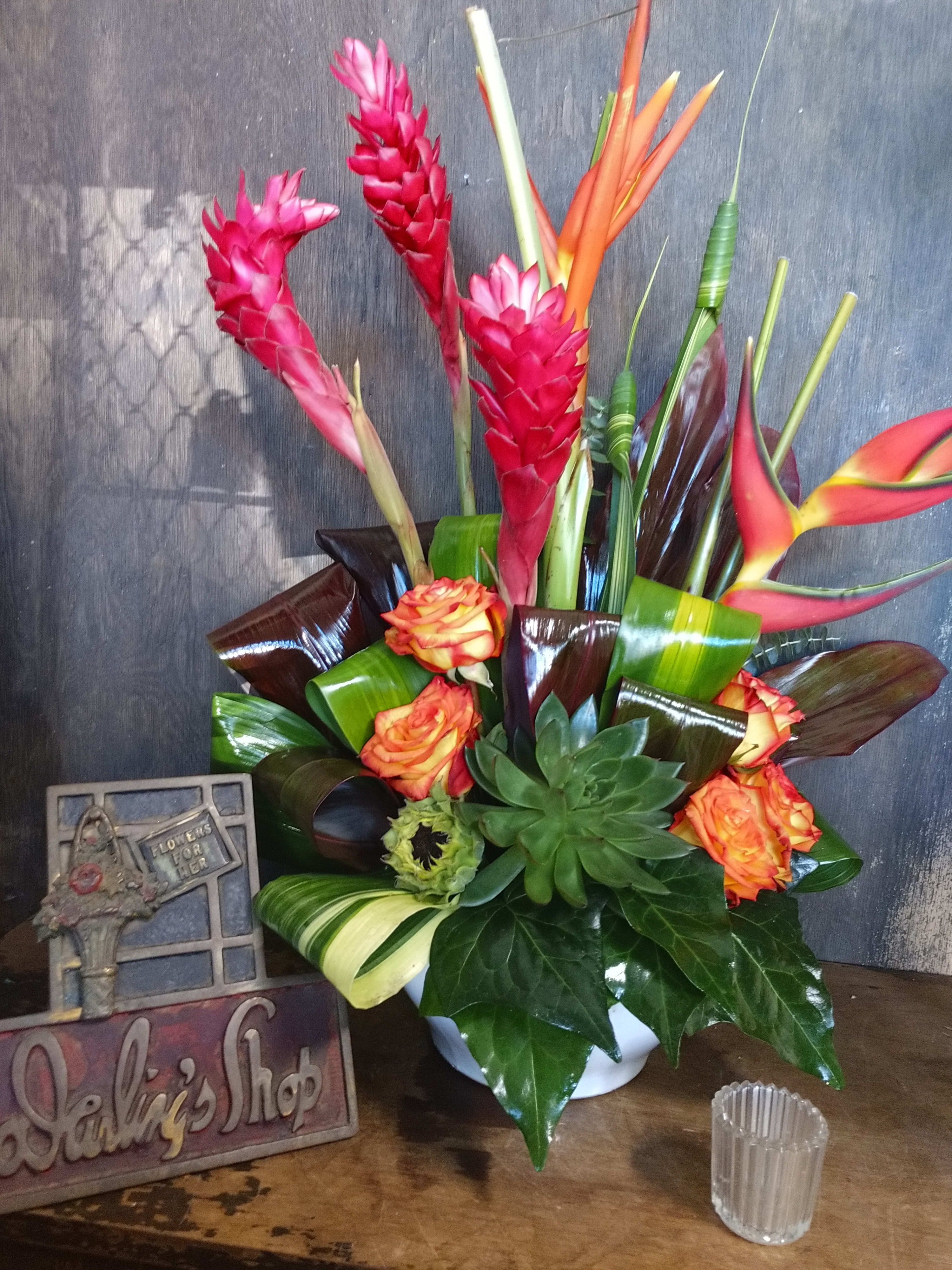 Tropical bouquet with pink ginger, orange heliconia, roses, and succulents in a white vase