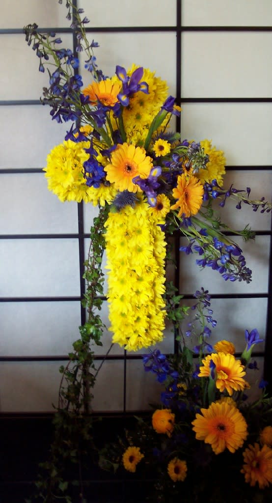 Cross-shaped floral arrangement with yellow and orange daisies and blue flowers