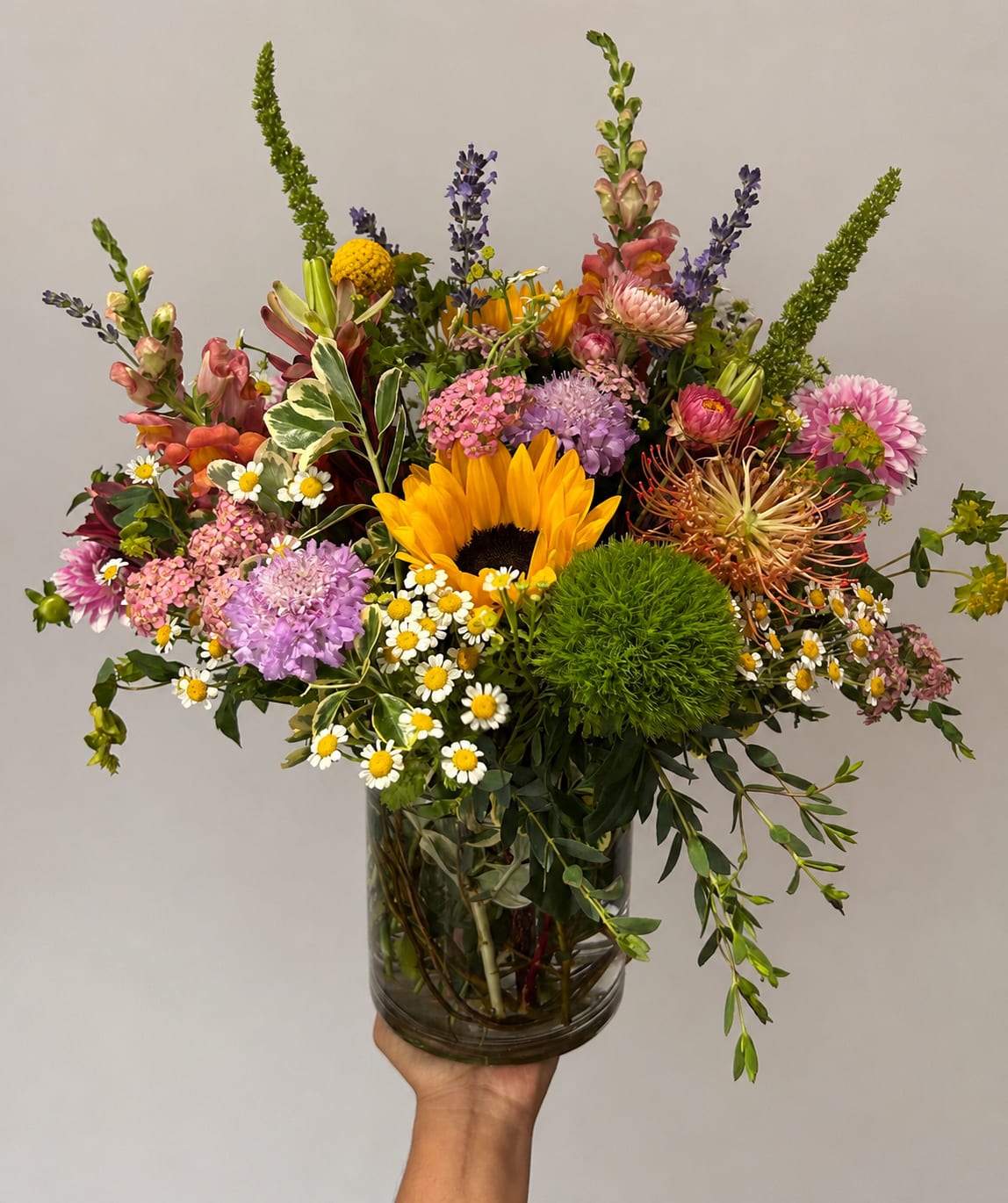 Mixed bouquet with a sunflower, daisies, and pink blooms in a glass vase