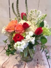 Mixed arrangement of peach roses, red blooms, and white flowers in a clear glass vase
