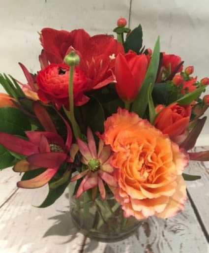 Compact red and orange flower arrangement in a clear glass cylinder vase