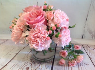 Short glass vase of light pink roses and carnations with extra pink spray roses beside it