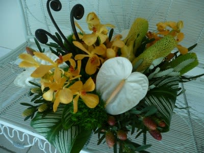 Low tropical arrangement with yellow orchids and white anthuriums among bold green foliage.