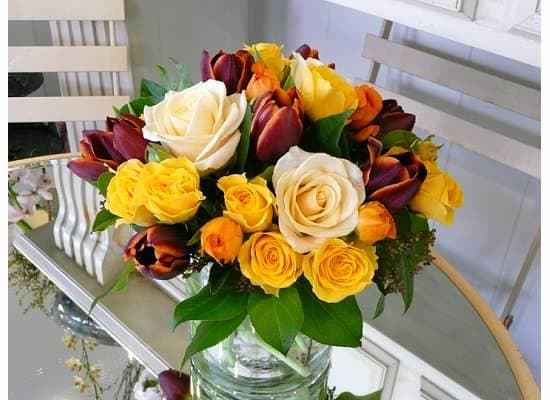 Round bouquet of white and yellow roses with burgundy tulips in a clear glass vase