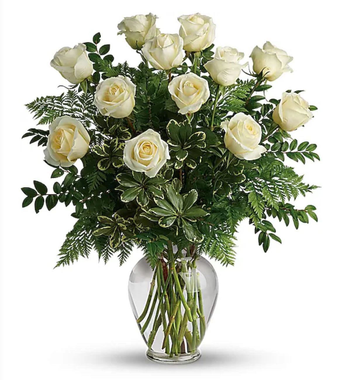 White roses arranged in a clear glass vase with mixed greenery