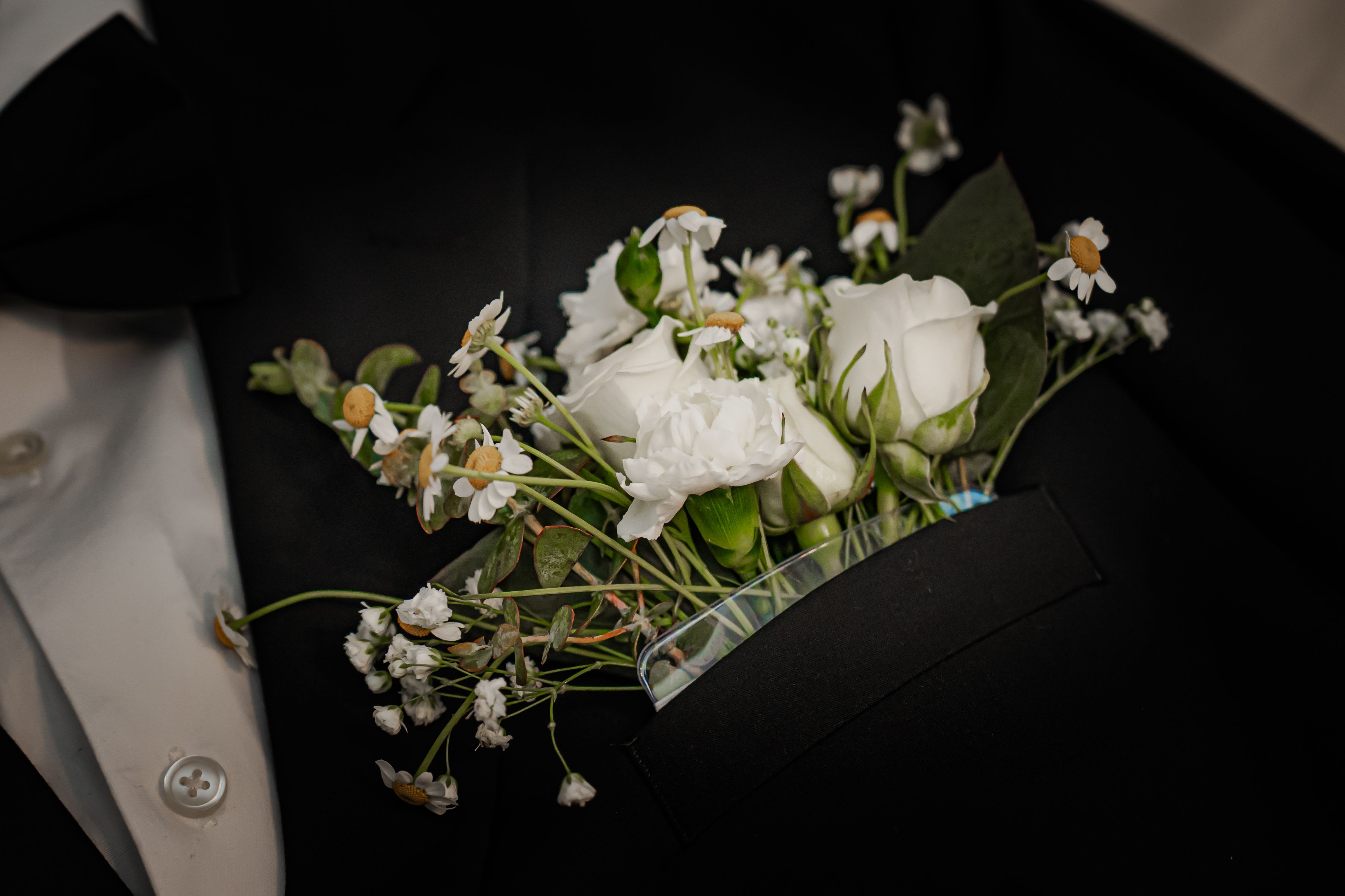 White boutonniere with small daisies and roses on a black suit jacket