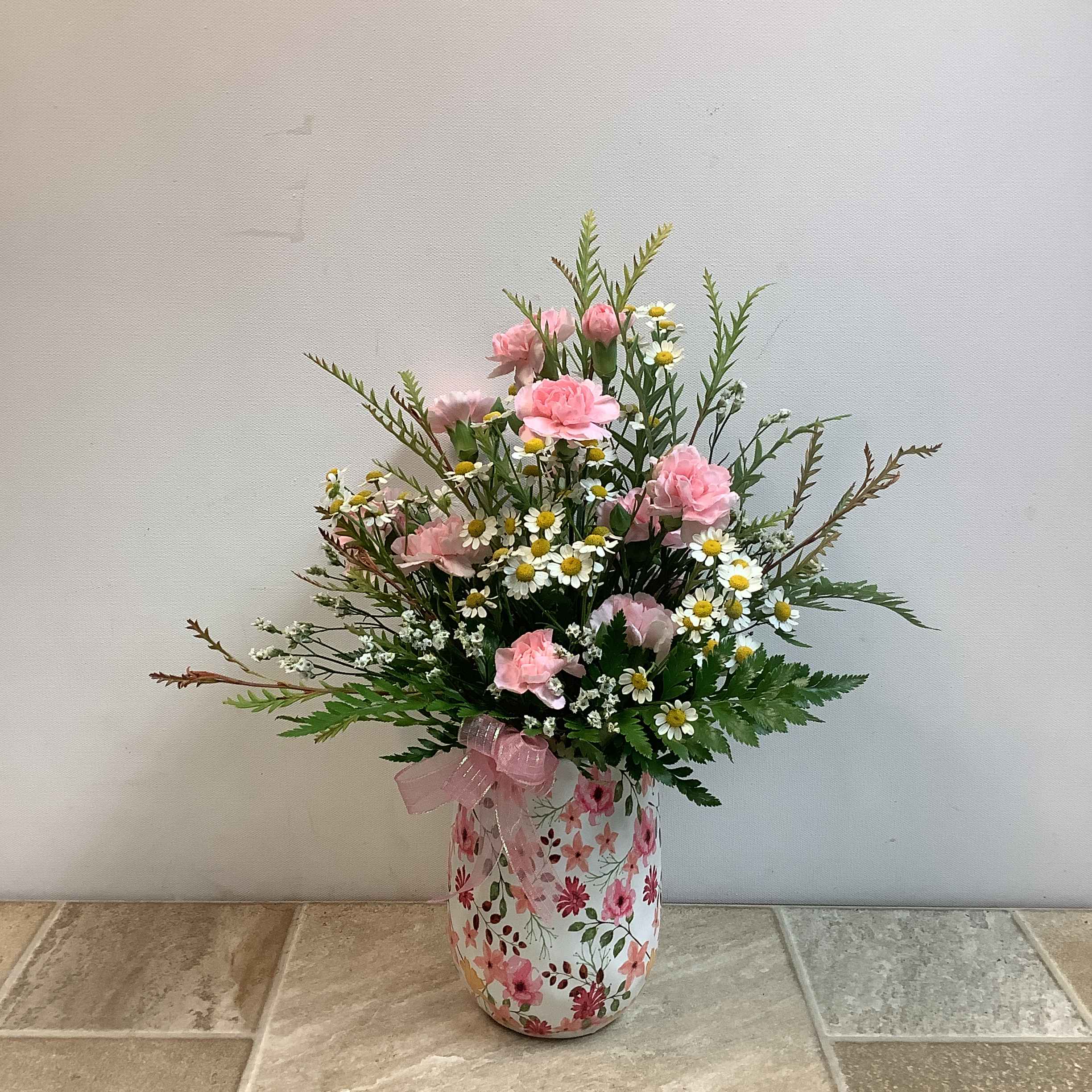 Pink carnations and small white daisies in a floral vase with a pink ribbon