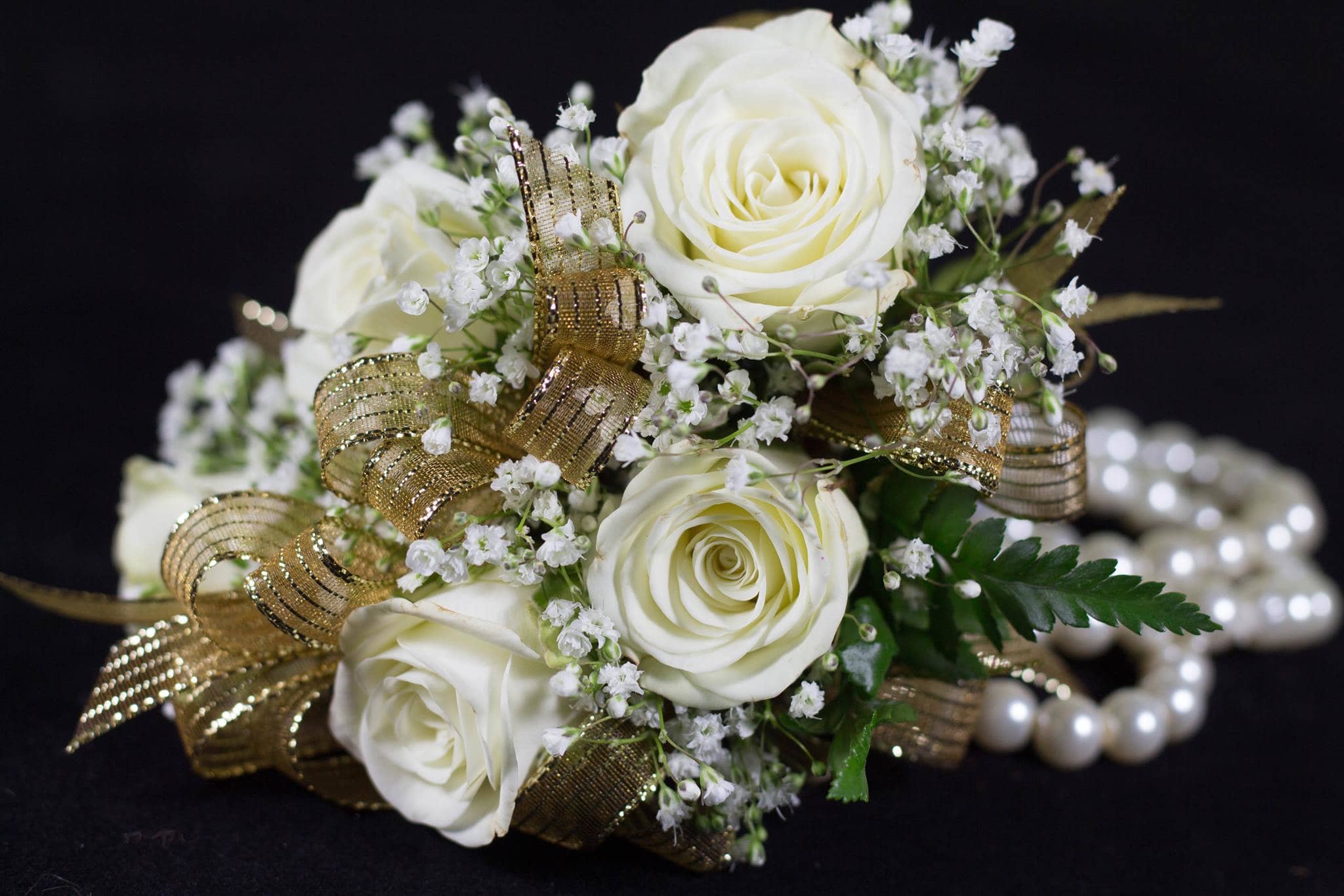 White rose bouquet with baby's breath and gold ribbon on a pearl bracelet