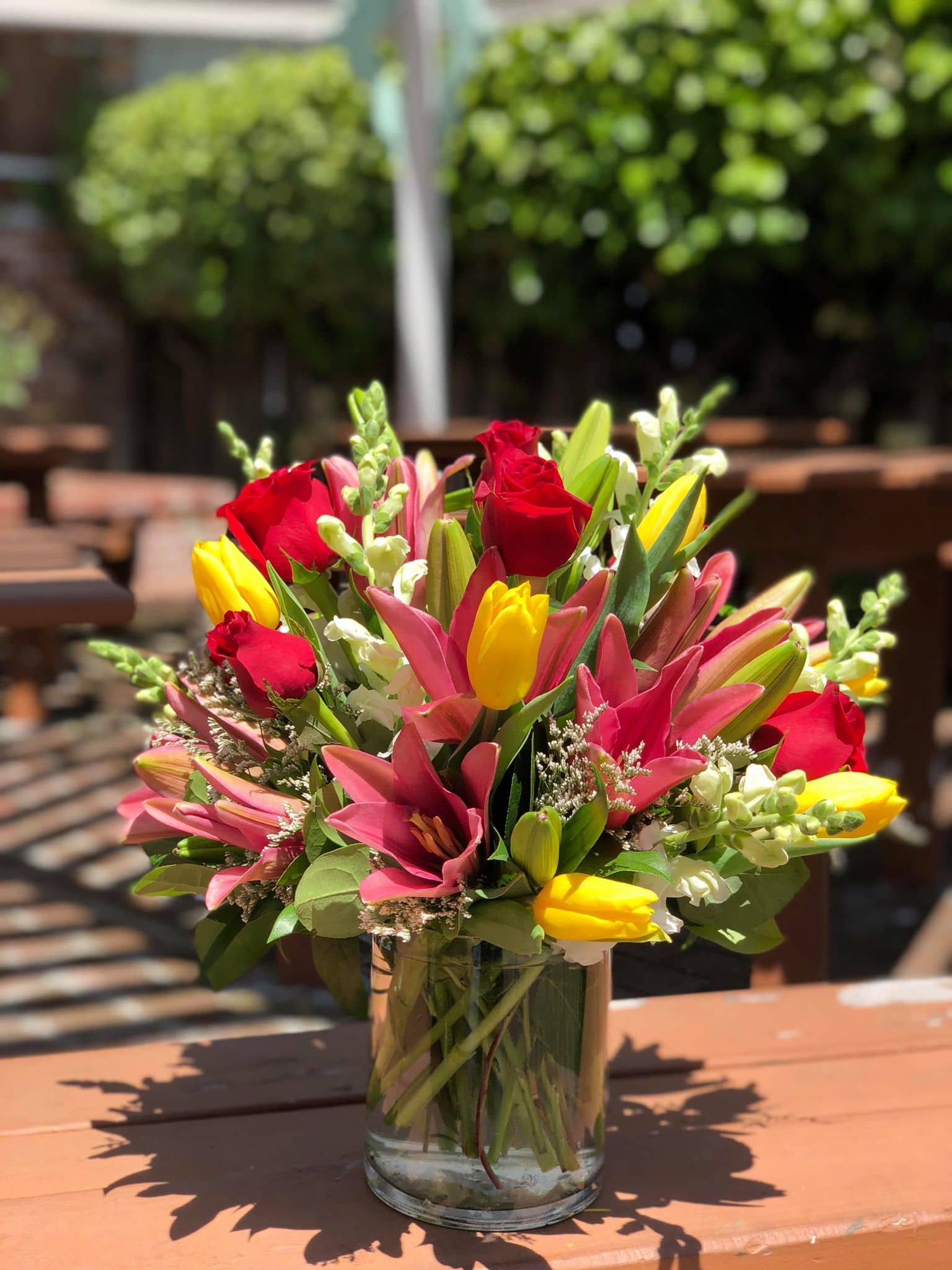 Mixed bouquet of red roses, pink lilies, and yellow tulips in a glass vase