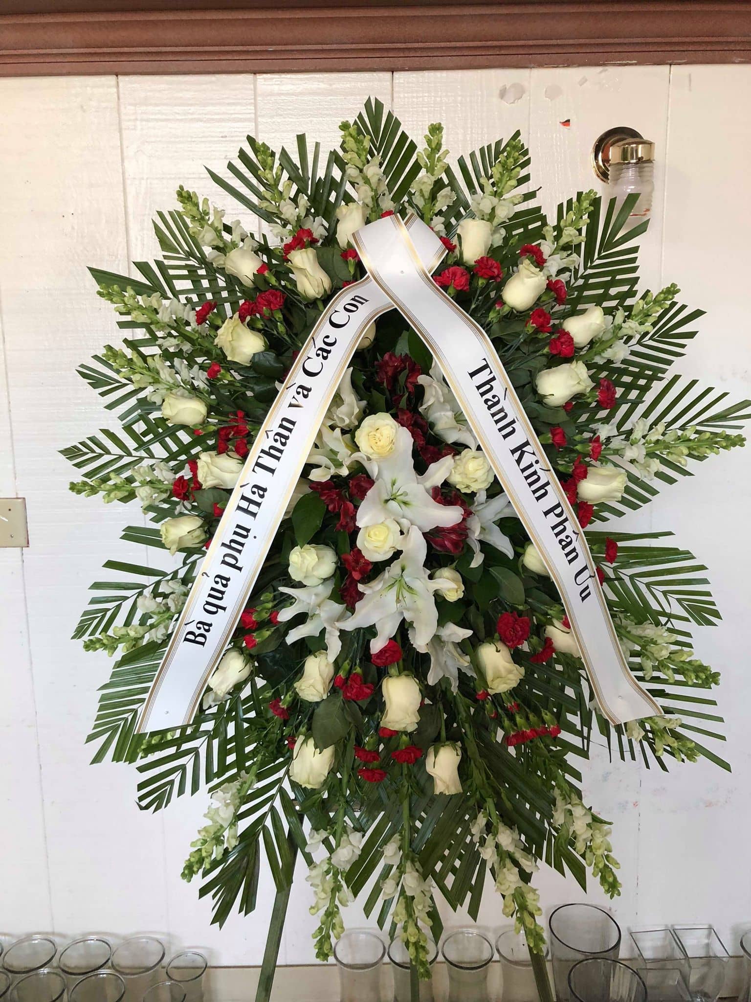 Standing funeral wreath with white roses, lilies, and red carnations