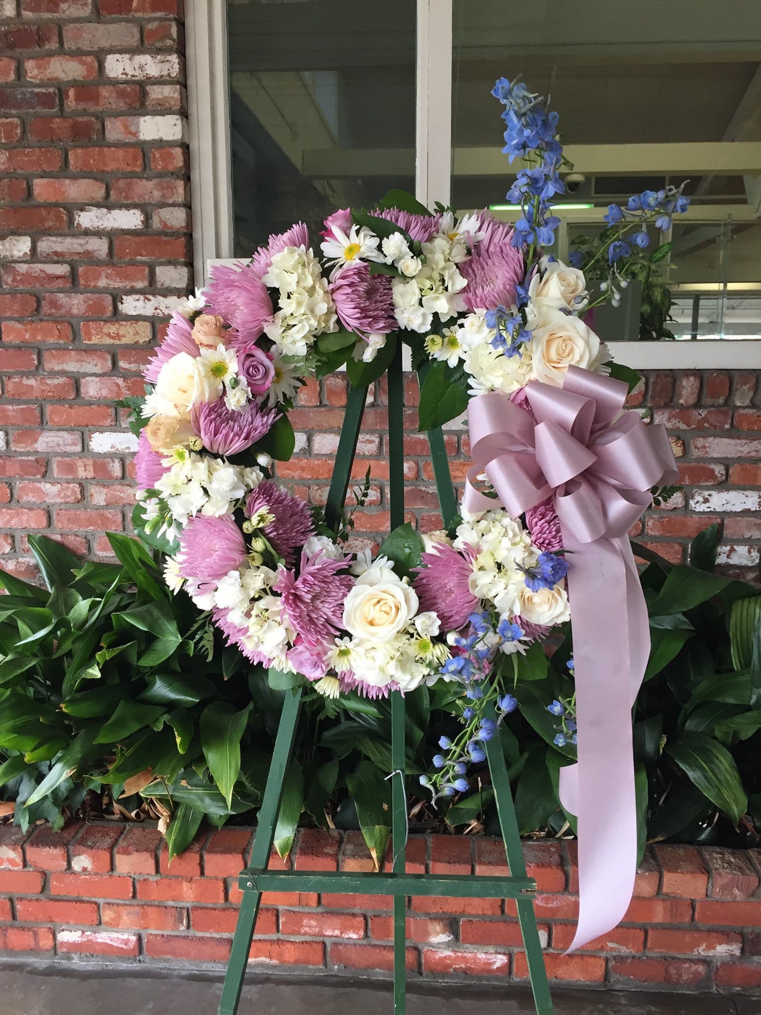 Floral wreath on an easel with pink, white, and blue flowers and a lavender ribbon