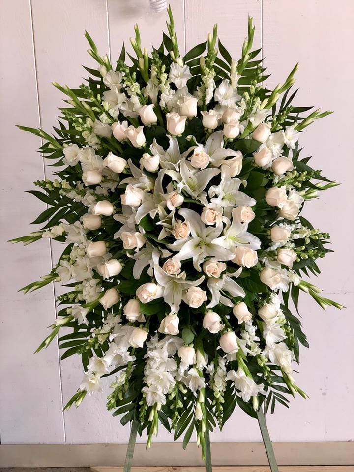 Large white funeral spray with roses and lilies on a stand