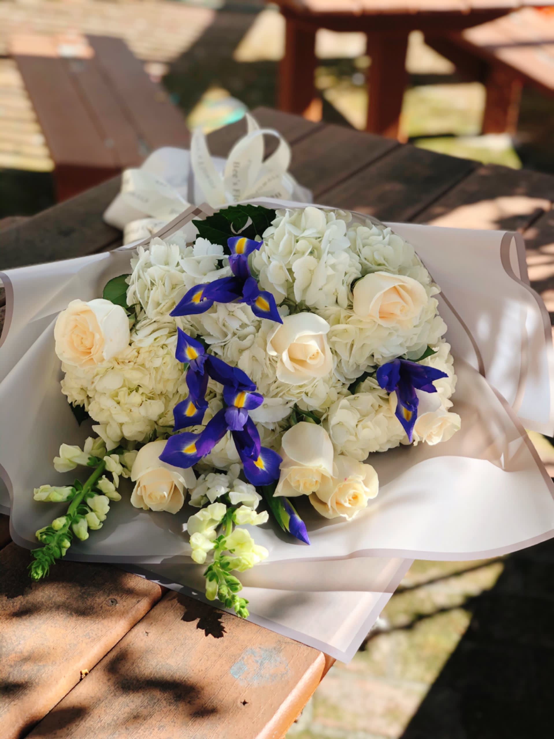 Bouquet of white flowers with cream roses and blue irises in pale wrapping