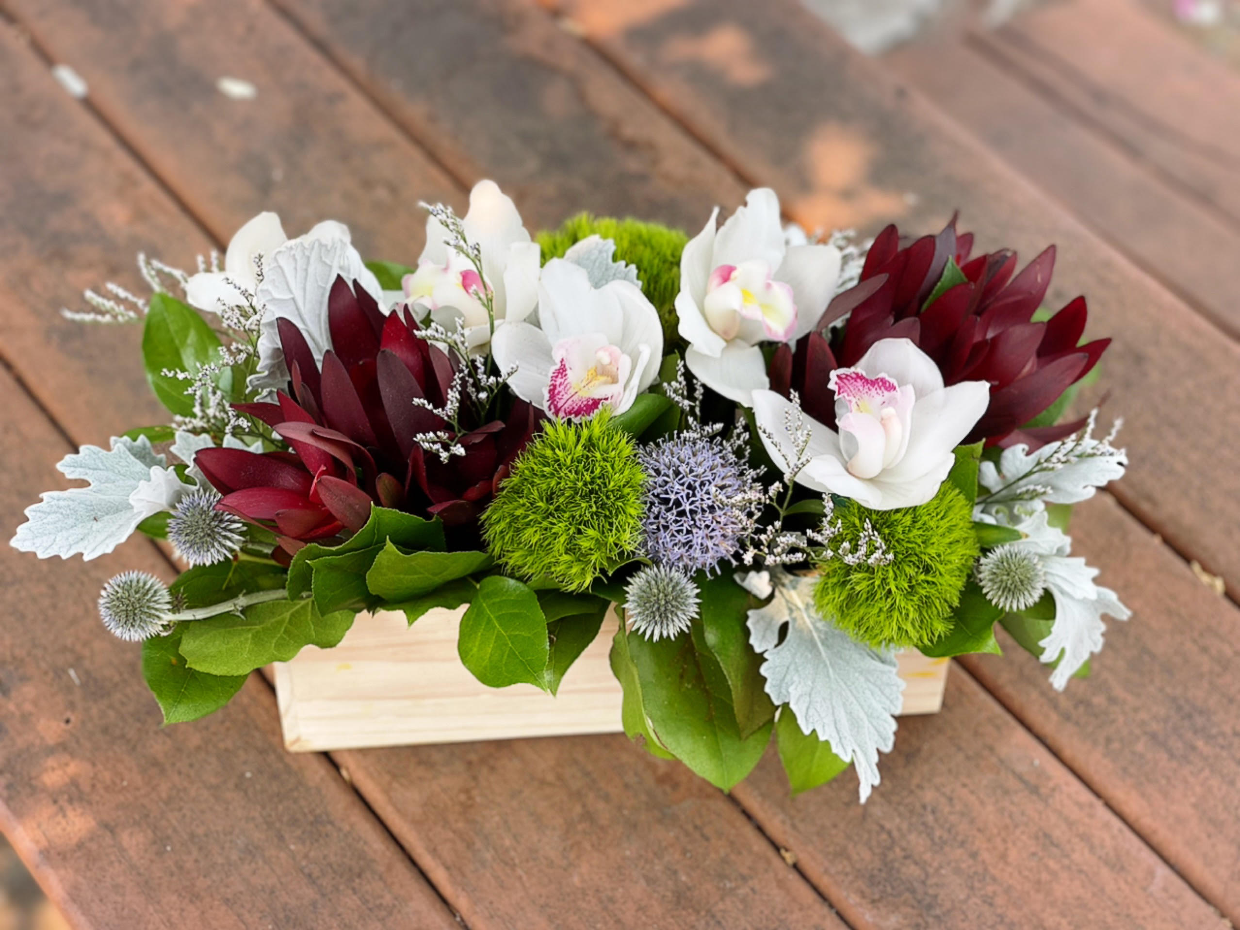 White orchids and burgundy flowers arranged in a wooden box