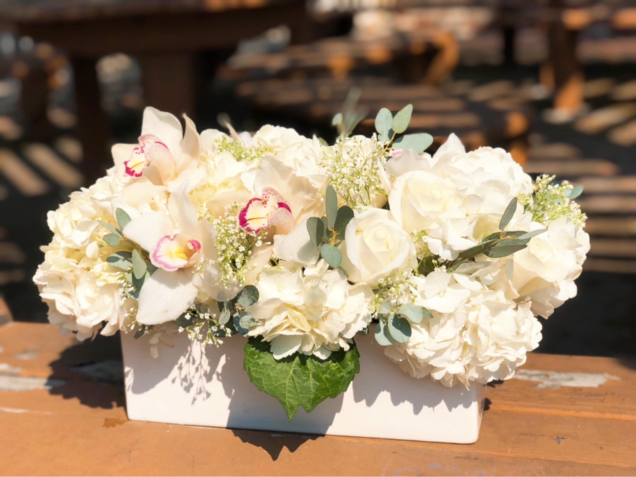 White floral arrangement in a rectangular vase with orchids and roses
