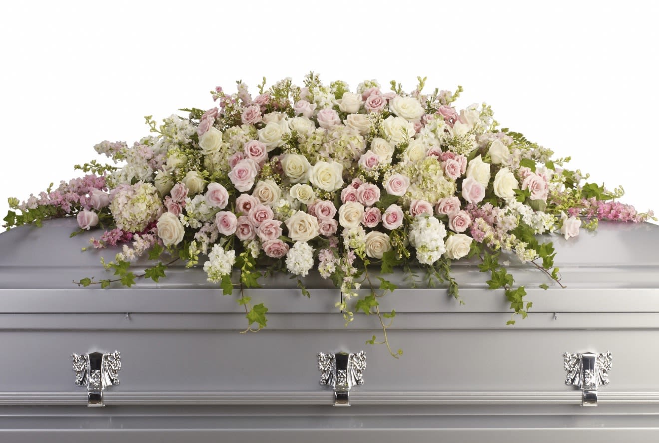 Always adored Casket Spray - A soft, layered casket spray that speaks to gentle remembrance-this flower arrangement is designed for sympathy and funeral services where tenderness and dignity matter. The arrangement combines clusters of white and blush roses, pale hydrangea, and small filler blooms to create a calm, comforting presence that helps express love and farewell for the person you're honoring.  Carefully arranged in a broad, low profile to lie across the top of the casket, the design includes carnations and other delicate flowers nestled among trailing greenery that adds graceful movement around the edges. The mix of textures-from the full hydrangea heads to the velvety roses and petite fillers-creates a restrained, formal look appropriate for memorial services; dimensions and specific sizing are designed to provide full coverage and visual balance across the casket.  This spray is a meaningful way to say "always adored" to a loved one, giving mourners a focal expression of sympathy and respect. Please note placement is crafted for casket display; if you have special requests about size, placement, or personalization, let us know when ordering so we can ensure the arrangement fits the service and your wishes.