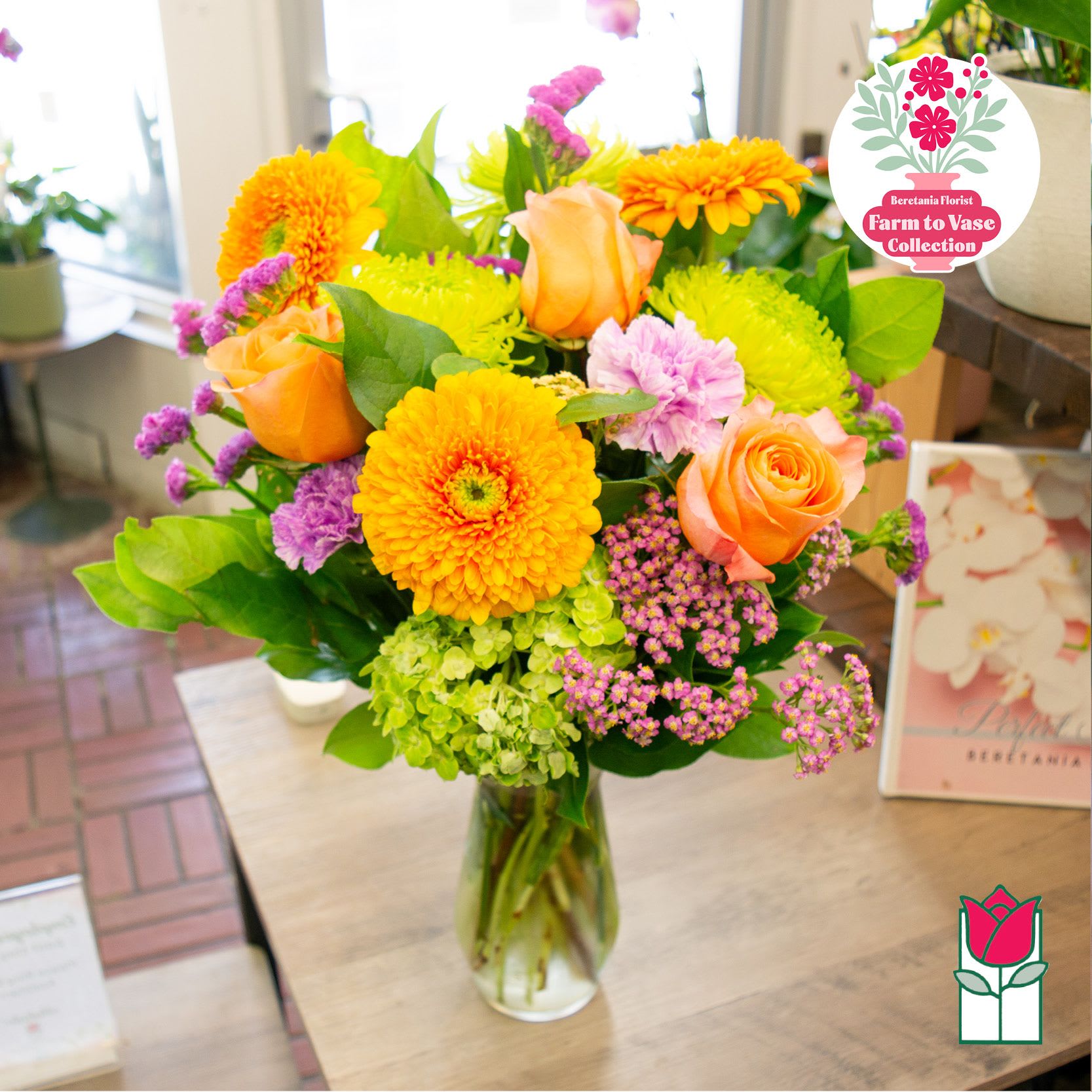 Mixed bouquet of orange roses, yellow blooms, and purple flowers in a glass vase
