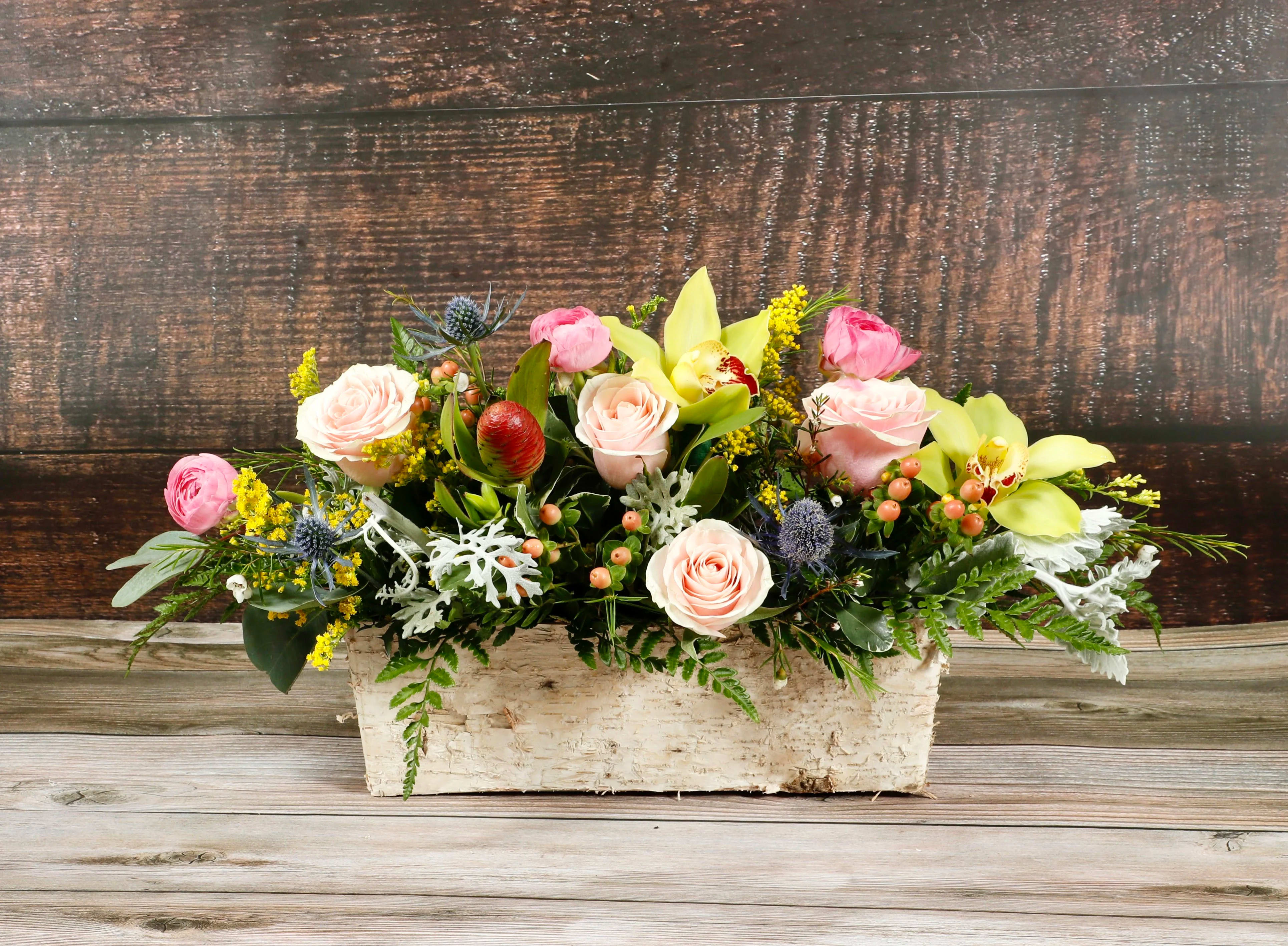 Low floral arrangement with pink roses and yellow orchids in a rustic white container
