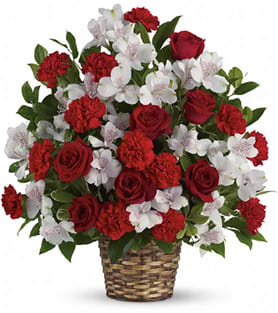 Red roses and carnations with white blossoms in a woven basket