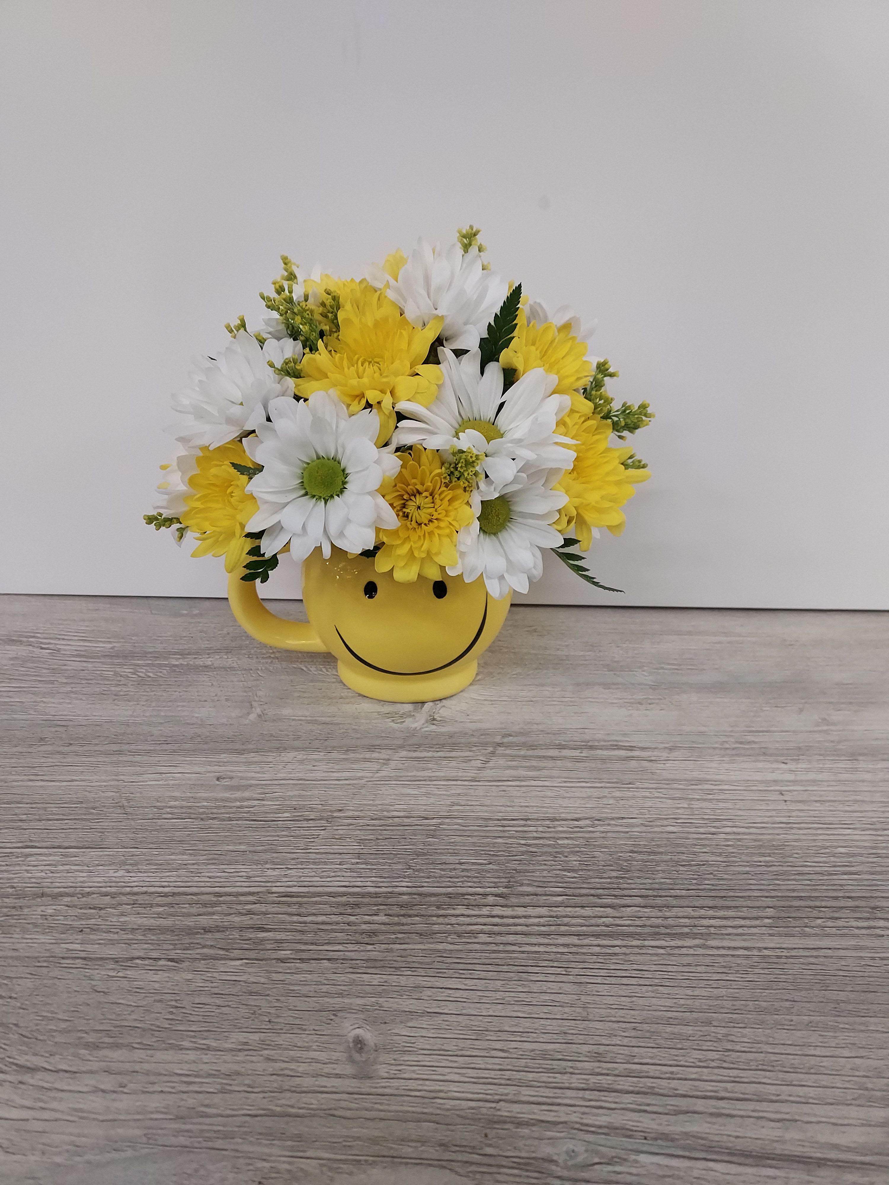 Yellow and white daisy and mum arrangement in a yellow smiley face mug
