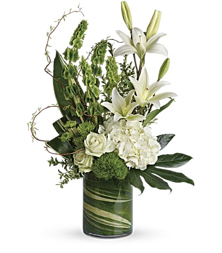 Tall white and green arrangement with lilies, hydrangea, roses, and bells of Ireland in a glass cylinder vase.