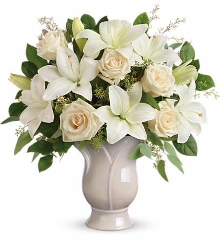 Arrangement of white lilies and cream roses in a pale ceramic pedestal vase